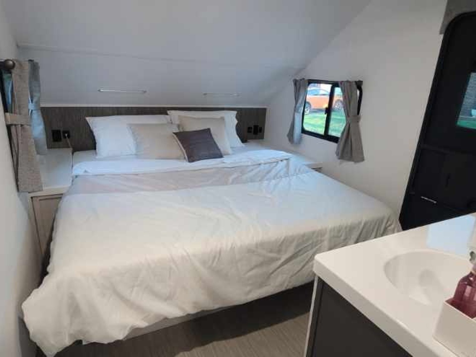 Cozy RV rental bedroom featuring a comfortable bed, window views, and a small vanity sink for convenience.. Travel Lite Evoke 2020
