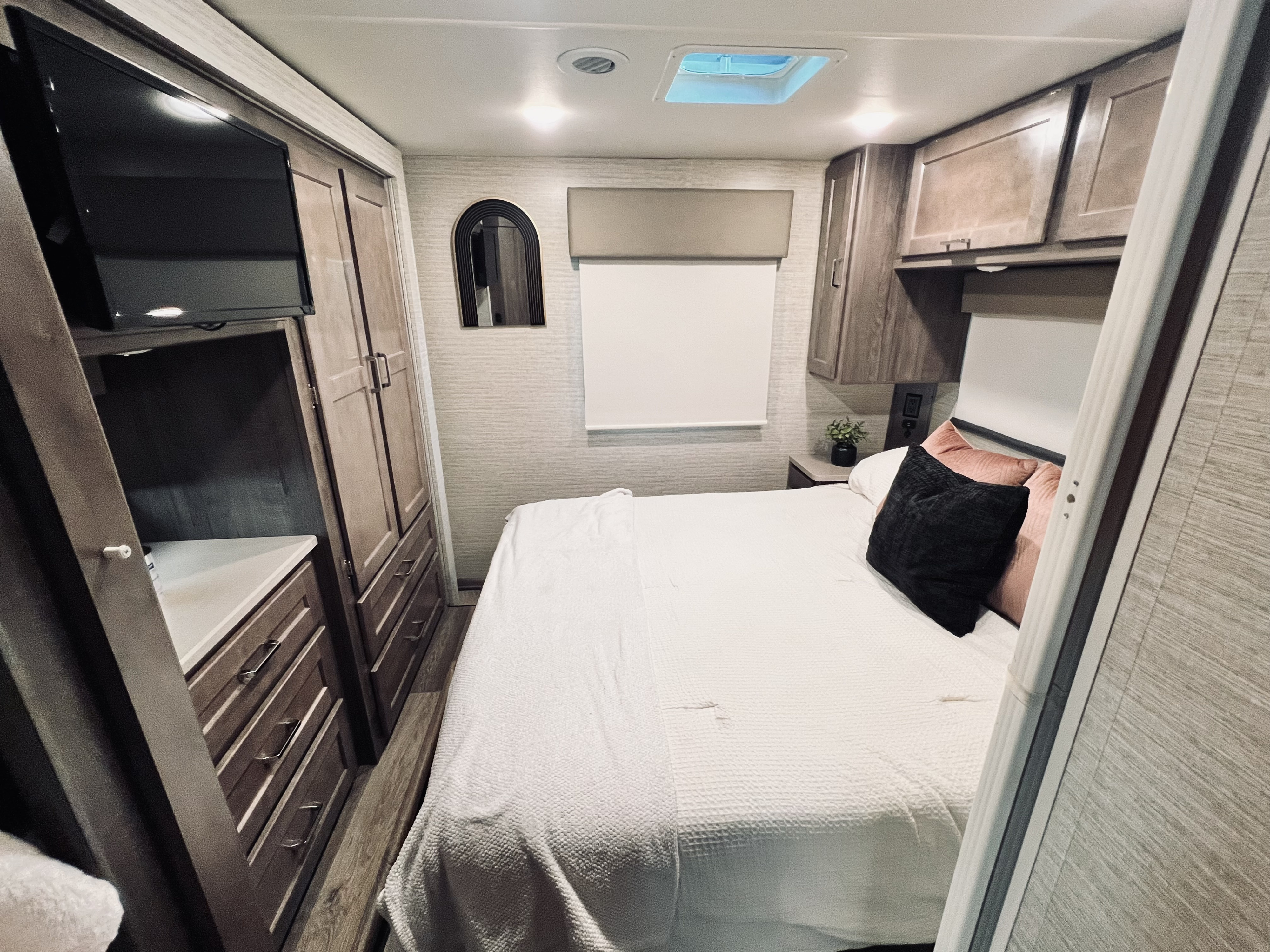 Inside an RV rental bedroom: cozy bed, flat-screen TV, modern cabinets, and a unique arched mirror.. Winnebago Minnie Winnie 2022
