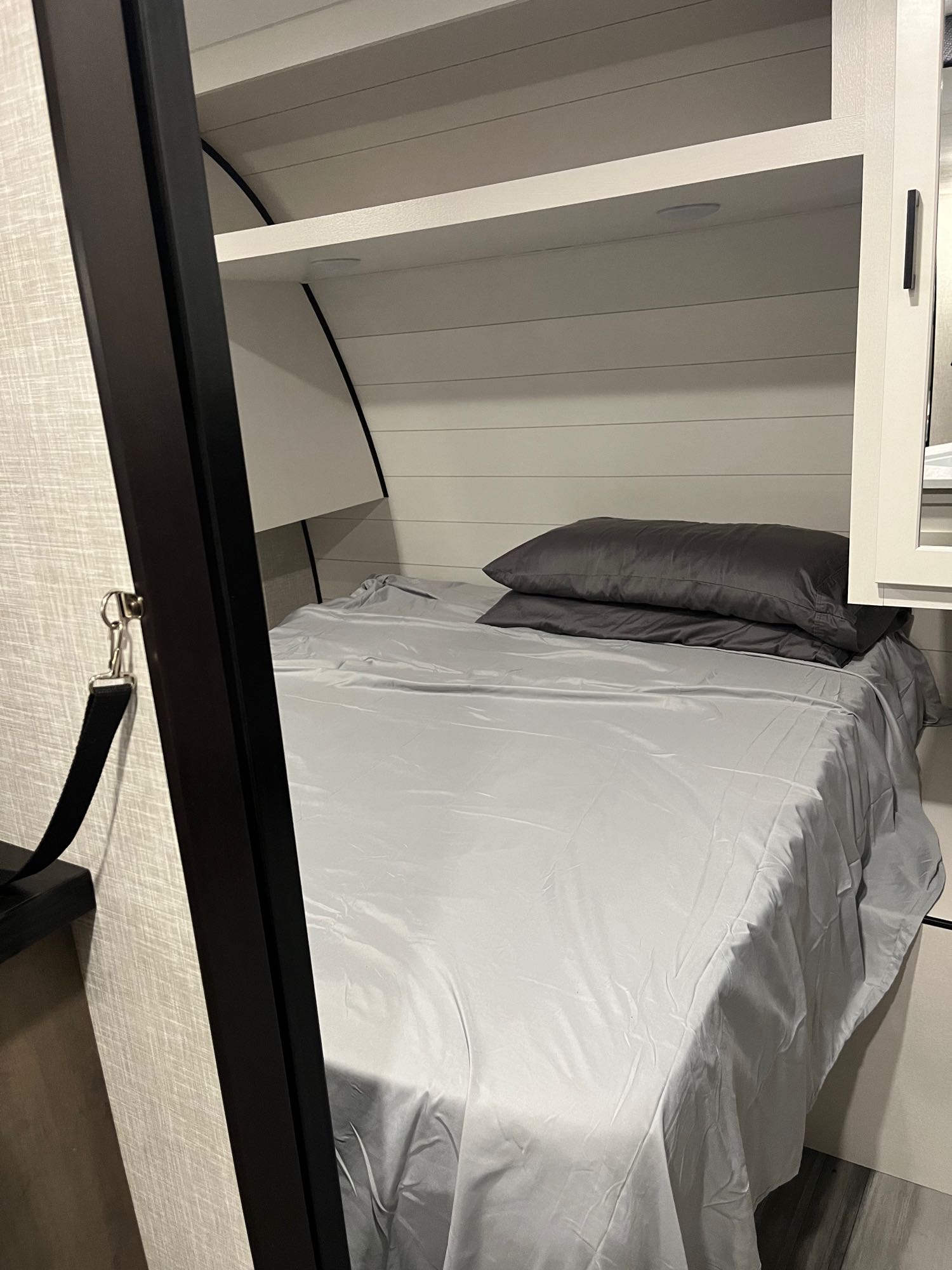 This cozy RV rental bedroom features a grey bed, shelf, and modern white plank walls, creating a perfect compact sleeping area.. Jayco JayFlight SLX 2024