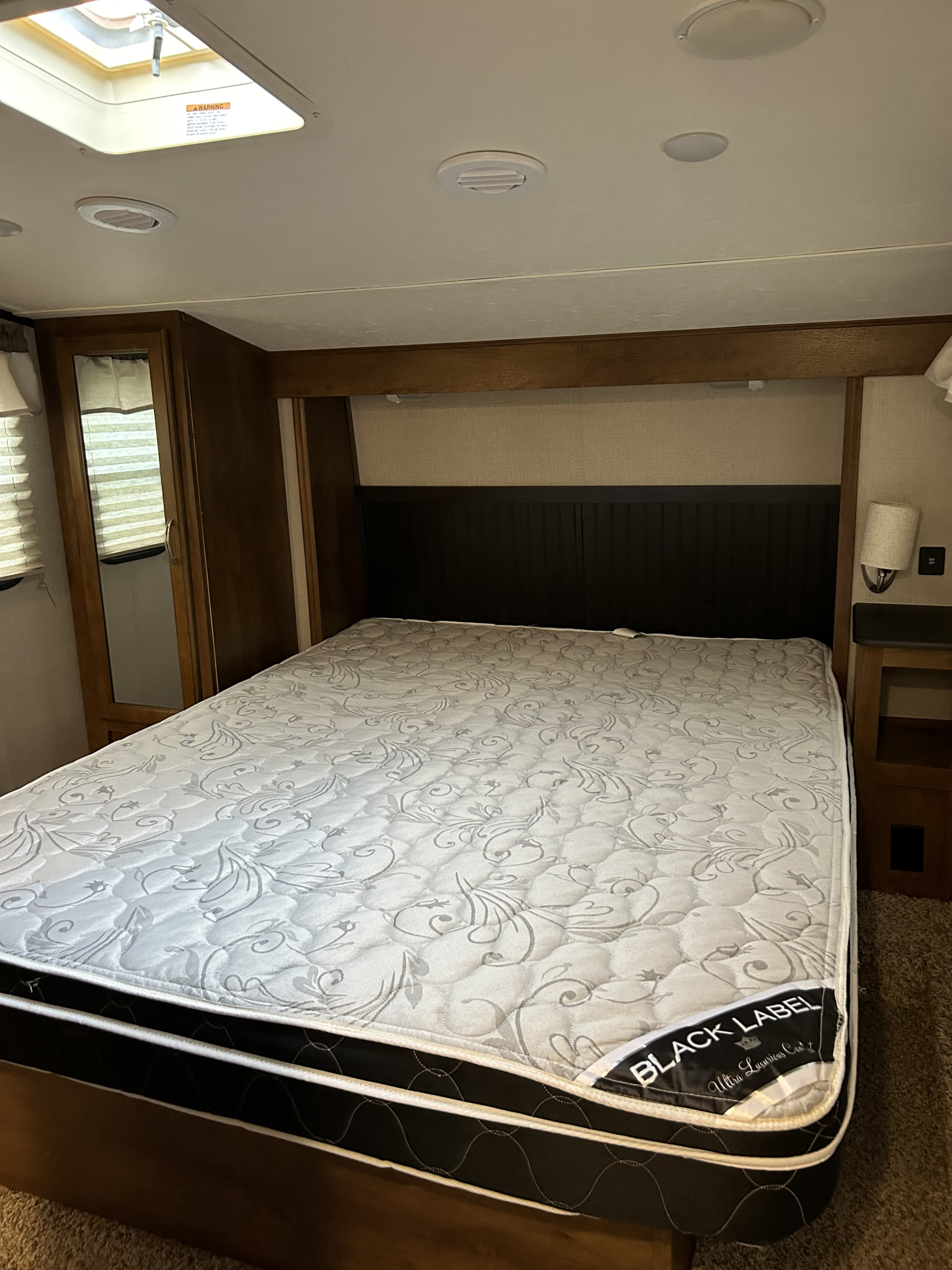 RV rental bedroom featuring a queen mattress, built-in storage, mirror, and ceiling skylight, offering a cozy retreat.. Forest River Coachmen Chaparral Lite 2019