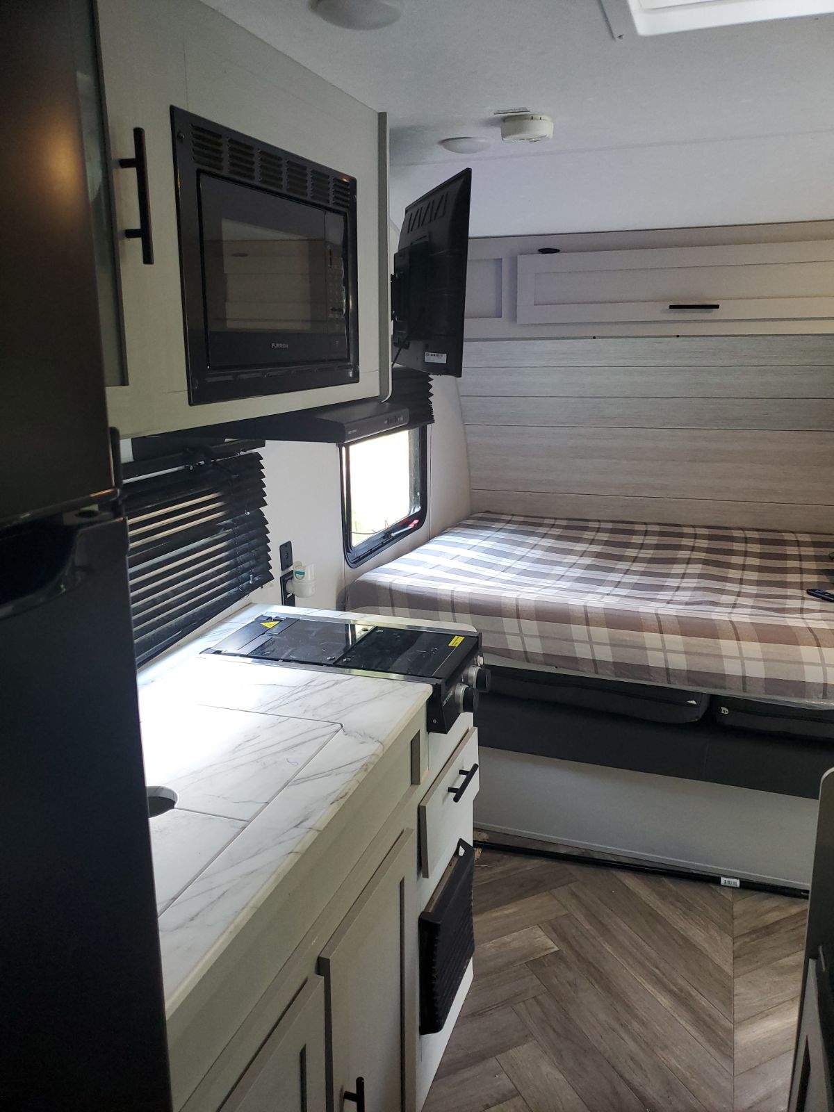 Inside this modern RV rental, find a compact kitchen with a microwave & stove, plus a cozy bed area and wall-mounted TV.. Forest River Salem FSX 2021