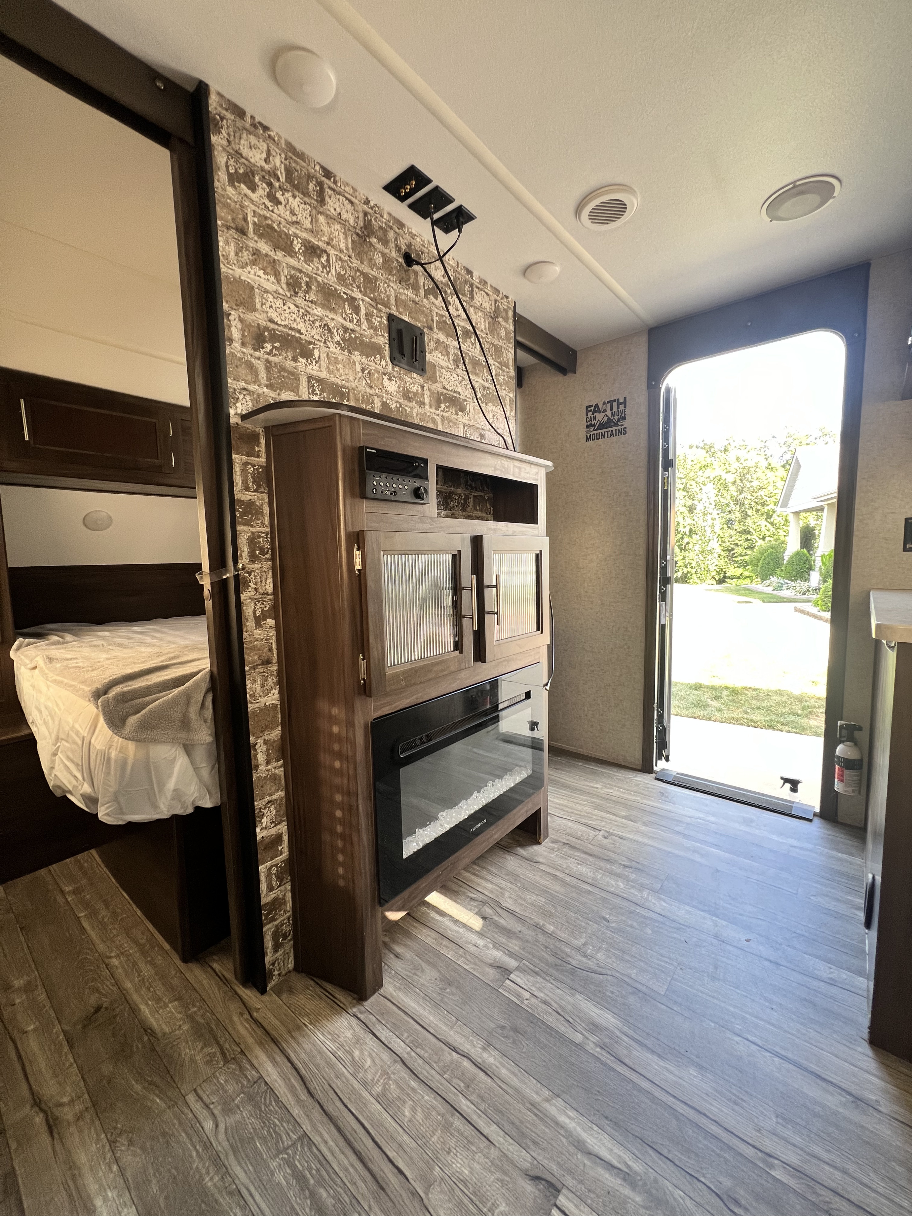 Cozy RV rental interior: bedroom, faux brick wall, media console with fireplace, and open door for outdoor views.. Forest River Cherokee Grey Wolf 2019