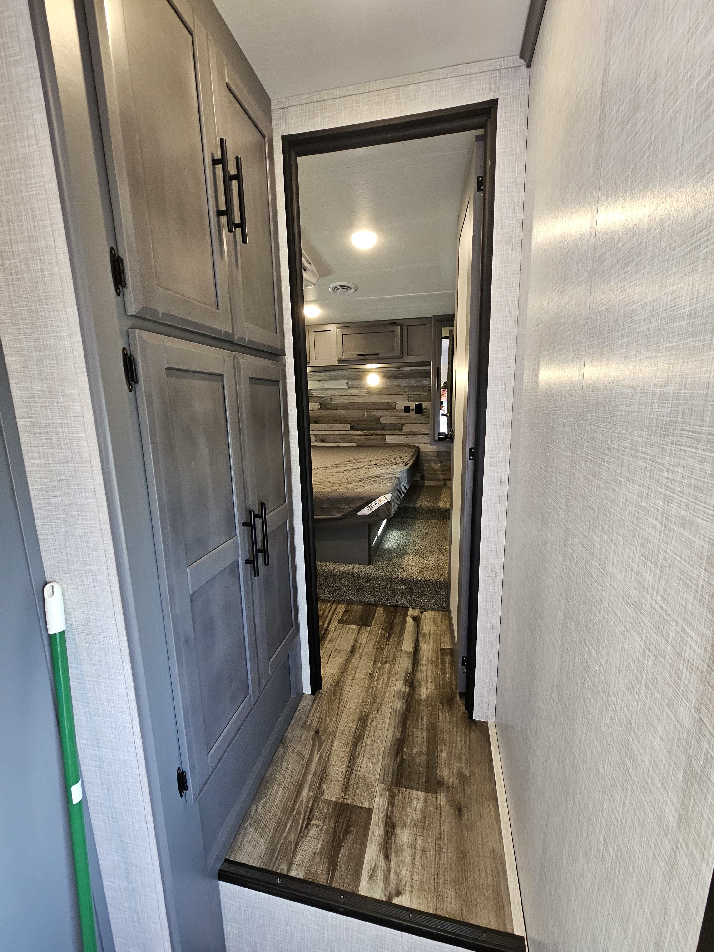 View of an RV rental's modern interior: a hallway with grey cabinets leading to a cozy bedroom with a wood accent wall.. Crossroads Volante 2023