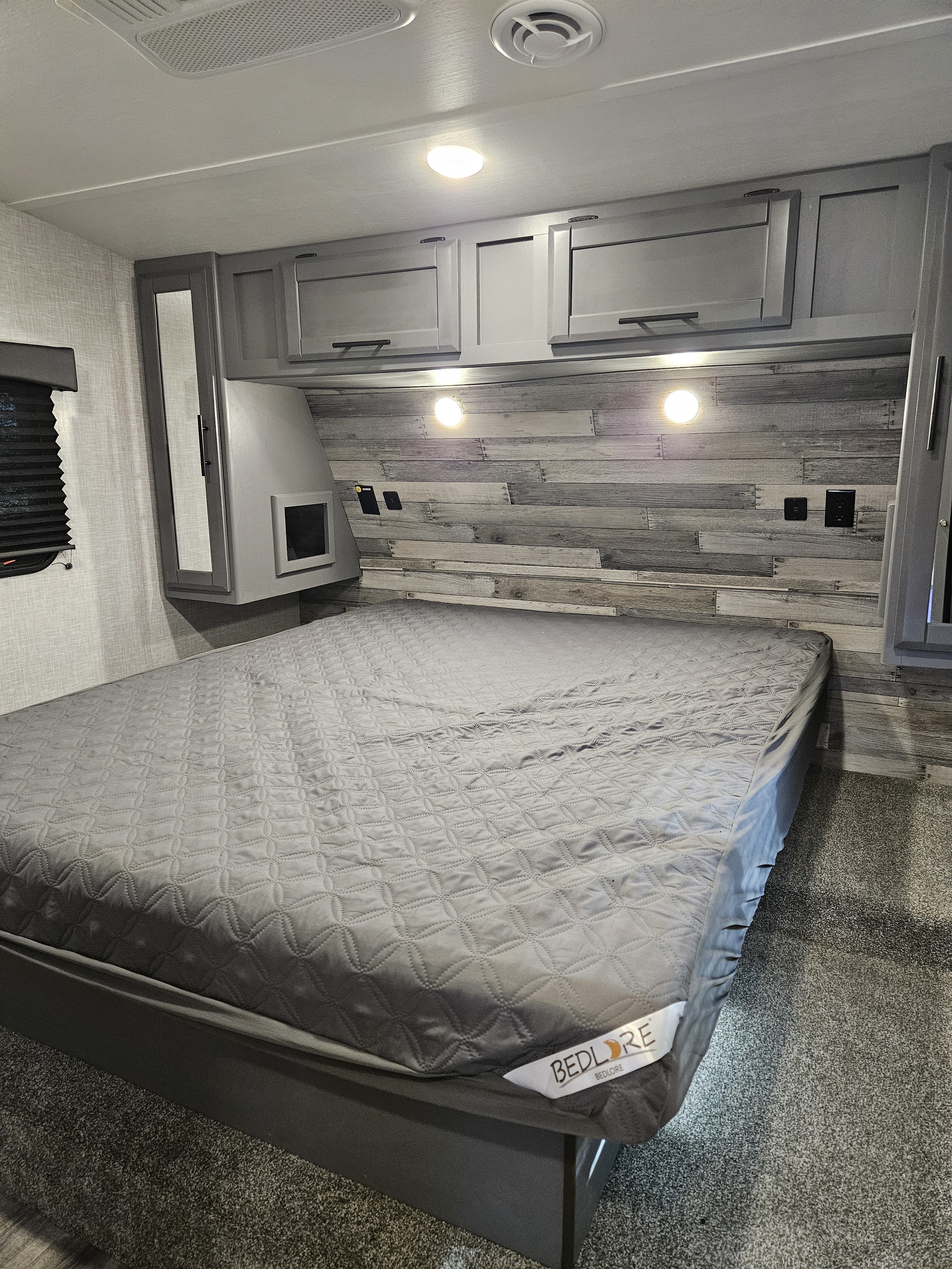 RV rental interior: a sleek grey bedroom with a quilted bed, wooden headboard, ample storage, and bedside charging points.. Crossroads Volante 2023
