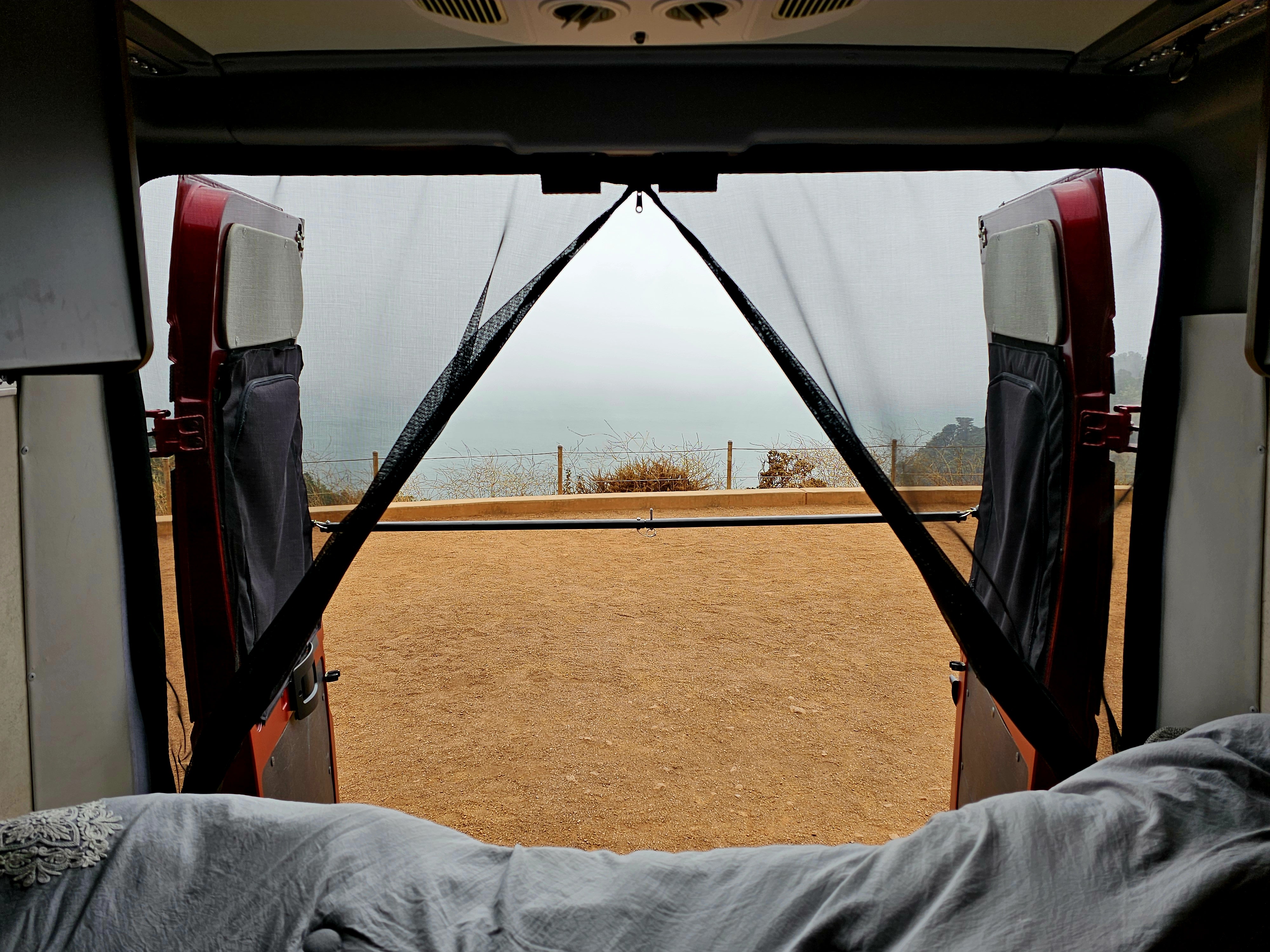 Experience an RV rental from within! Back doors open to a mesh screen, revealing a sandy area & a beautiful misty ocean view.. Winnebago Solis 2023