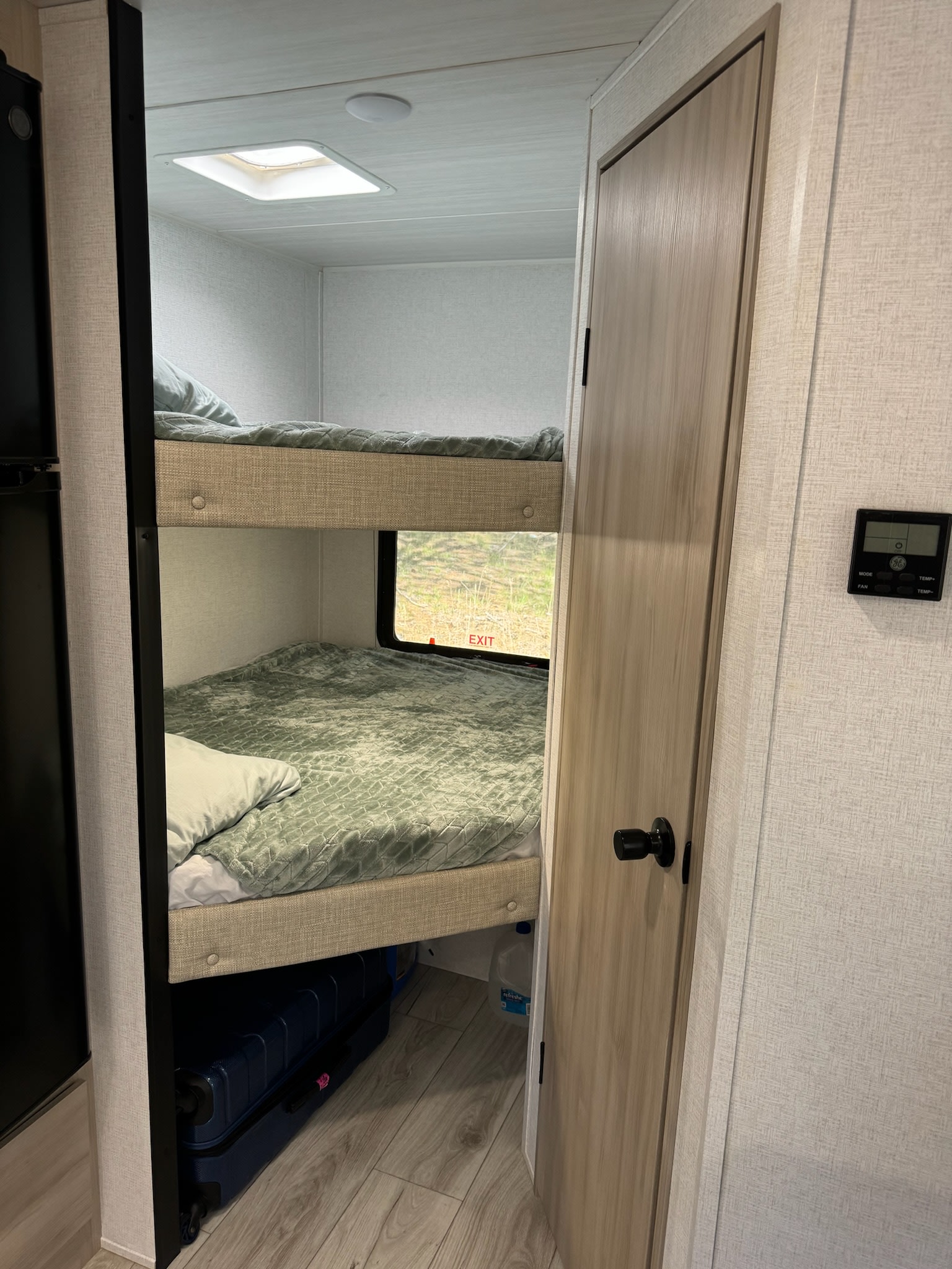 Cozy bunk beds inside an **RV rental**, with a door, window, and suitcase visible. Ideal for compact living.. East to West Della Terra 181 BHSLE 2024