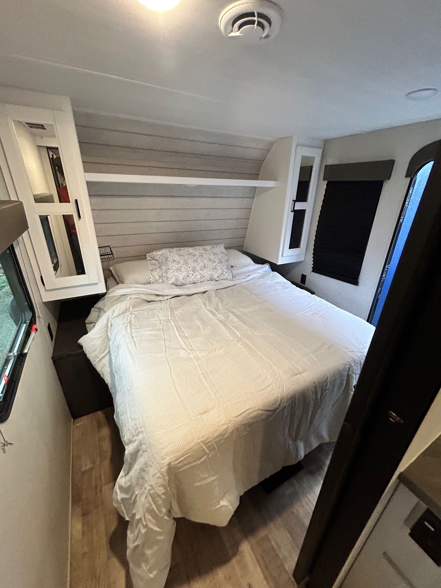 Experience comfort in this RV rental's cozy bedroom, featuring a large bed with white bedding, shiplap walls, and built-in storage.. Keystone RV Hideout 2022