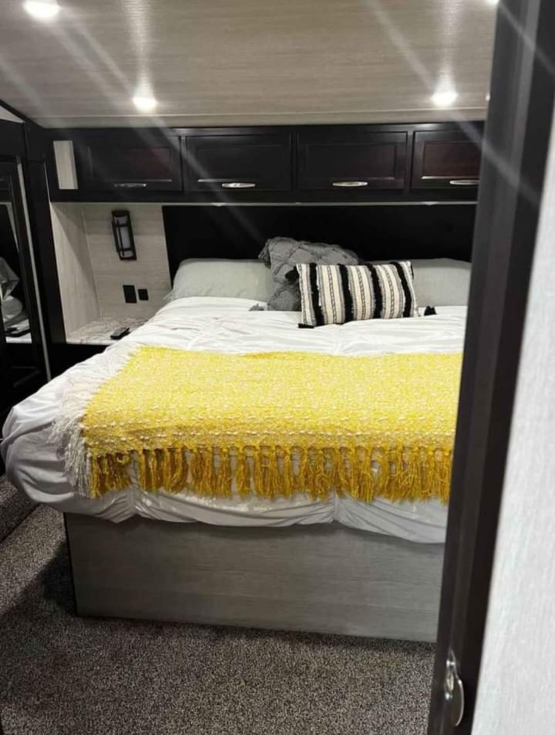 Cozy RV rental bedroom with white bed, yellow throw, and overhead storage. Ideal for a comfortable camper stay.. GENESIS MGM 2021