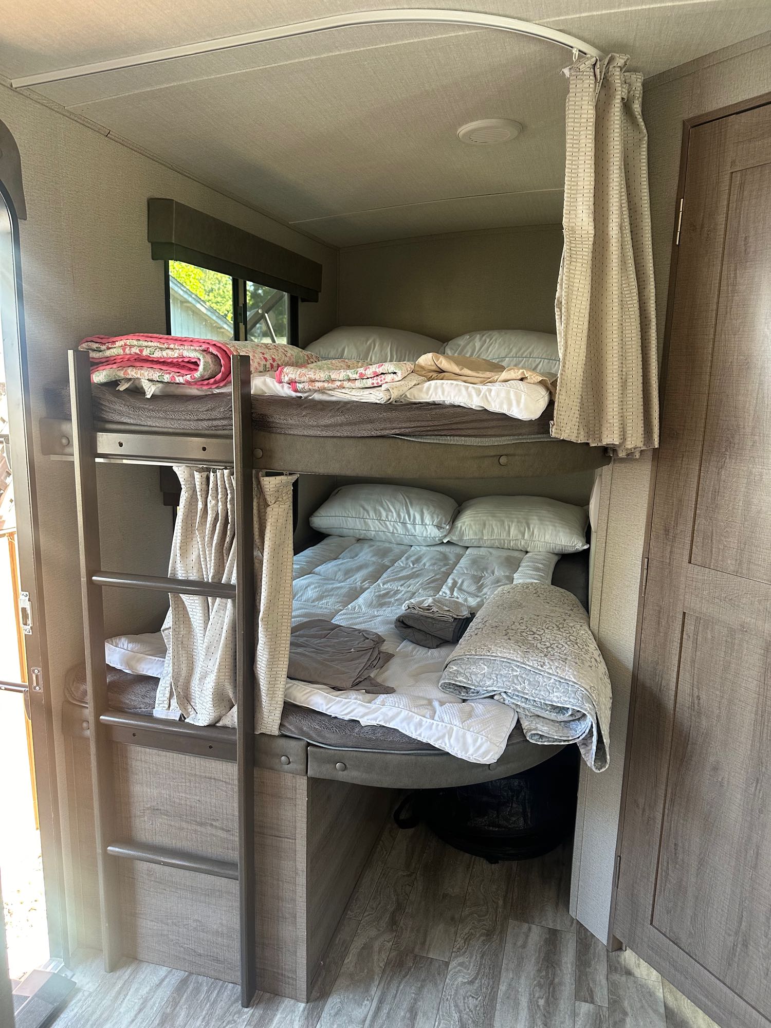 RV rental sleeping area: Two bunk beds, upper has pink quilt, lower has gray quilt. Ladder & privacy curtains are visible.. Grand Design Imagine 2020