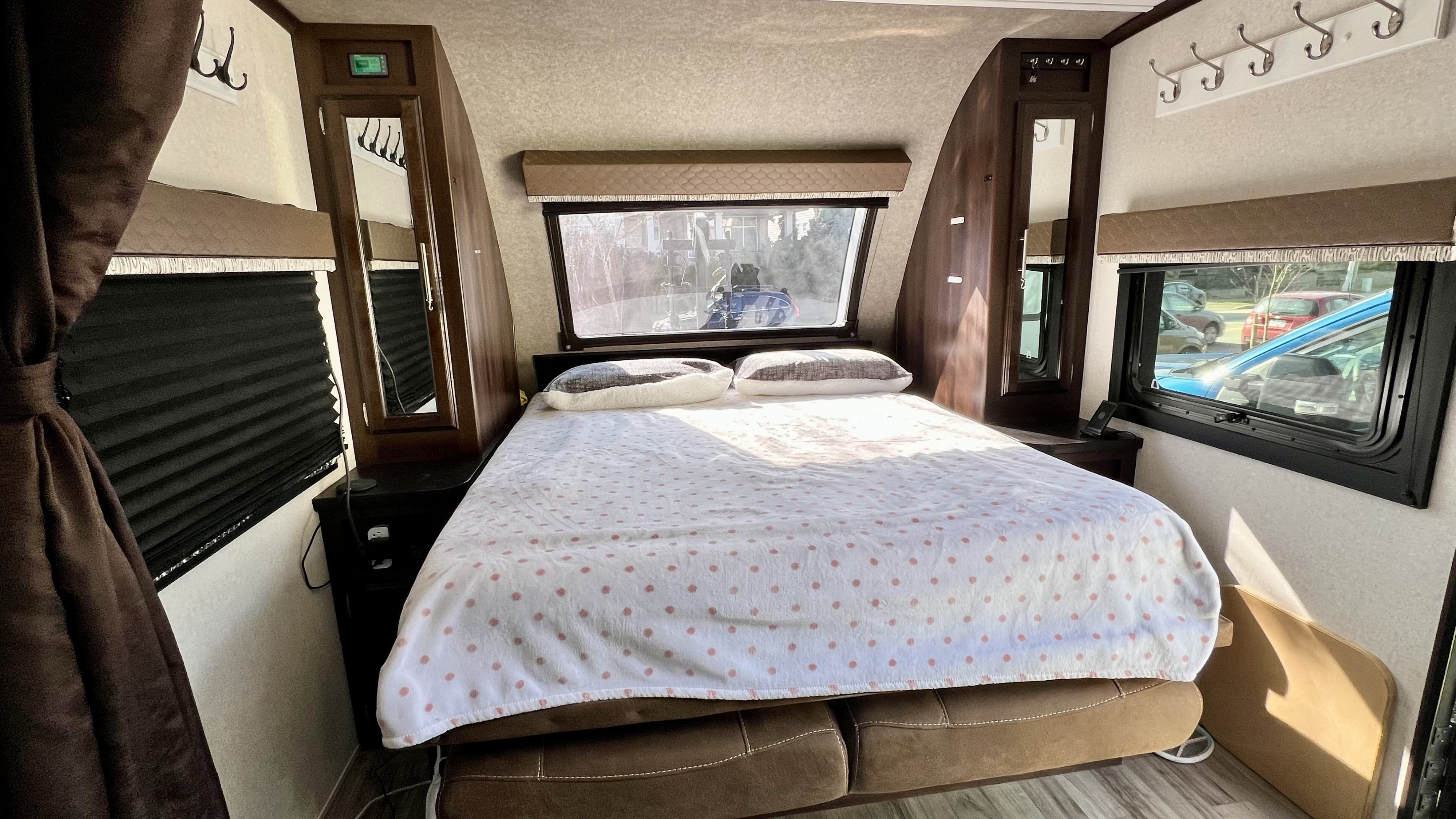 Interior of an RV rental bedroom showing a bed with a white and pink polka dot blanket, windows, and side cabinets.. Jayco White Hawk 2018