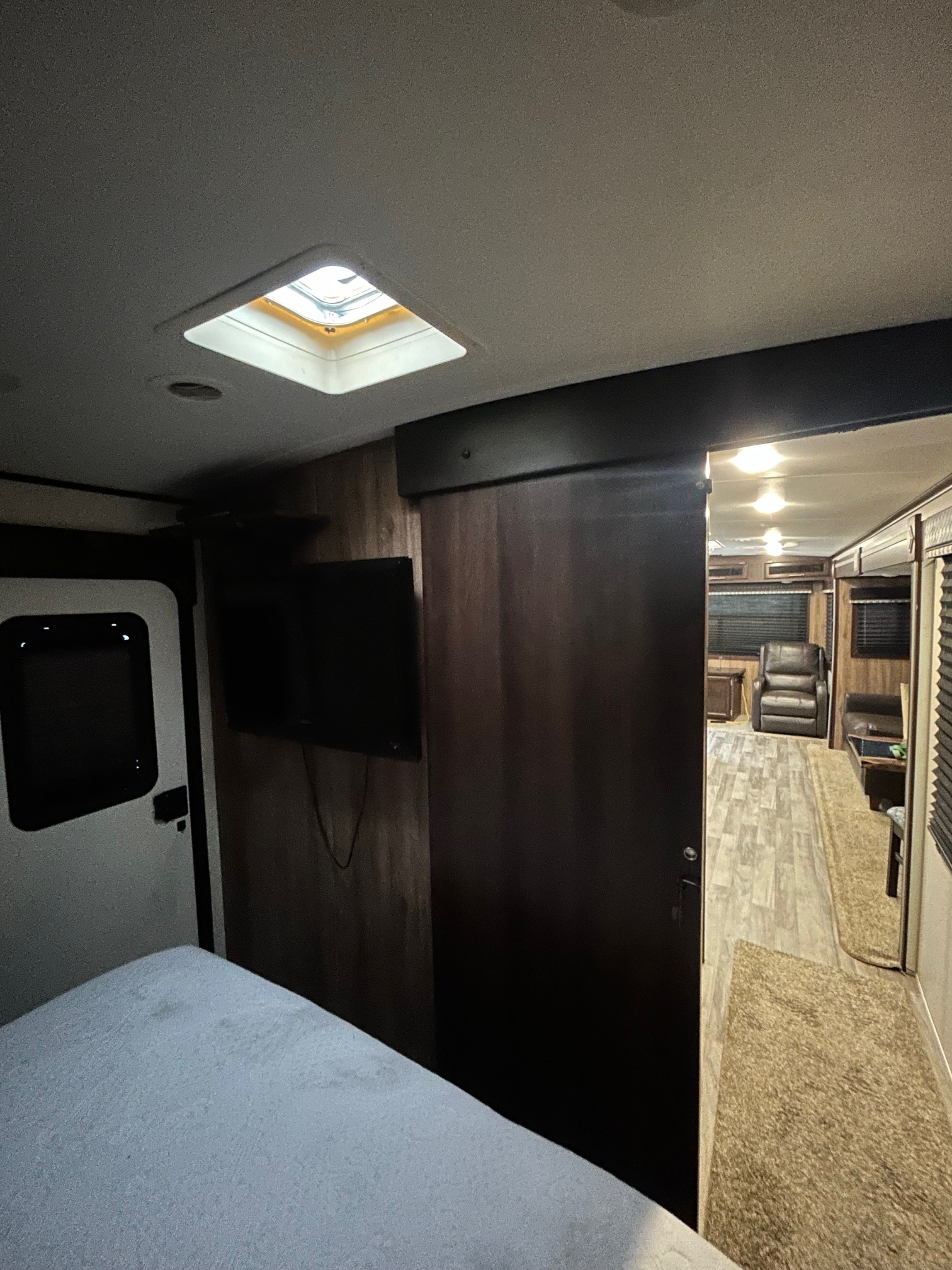 RV rental interior: bedroom with bed, TV, and skylight, opening to living area with recliners and wood flooring.. Jayco White Hawk 2019
