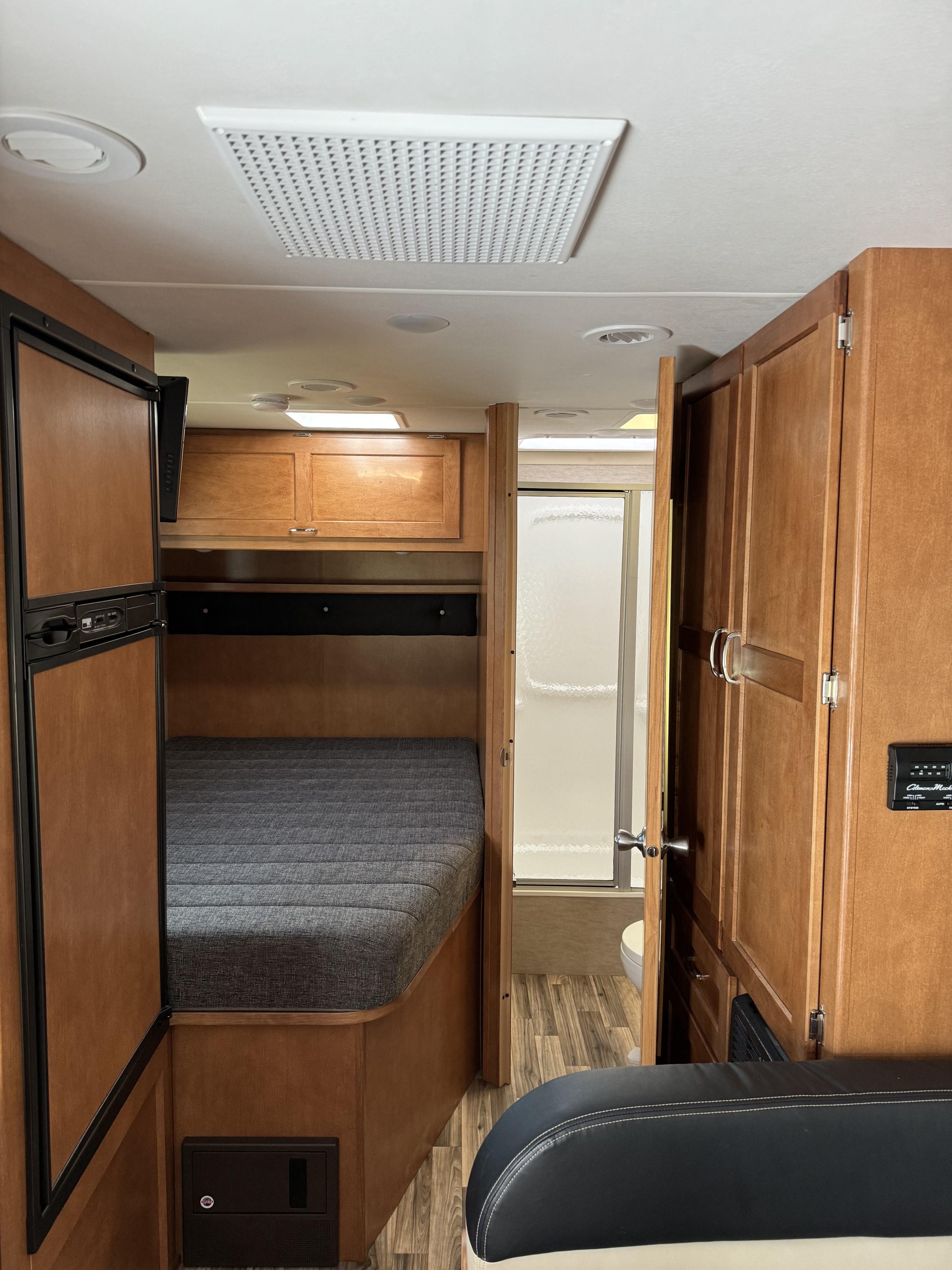 Inside this comfy RV rental: bedroom area with bed, fridge, overhead storage, and access to a compact bathroom. Perfect for travel.. Winnebago Spirit 2017