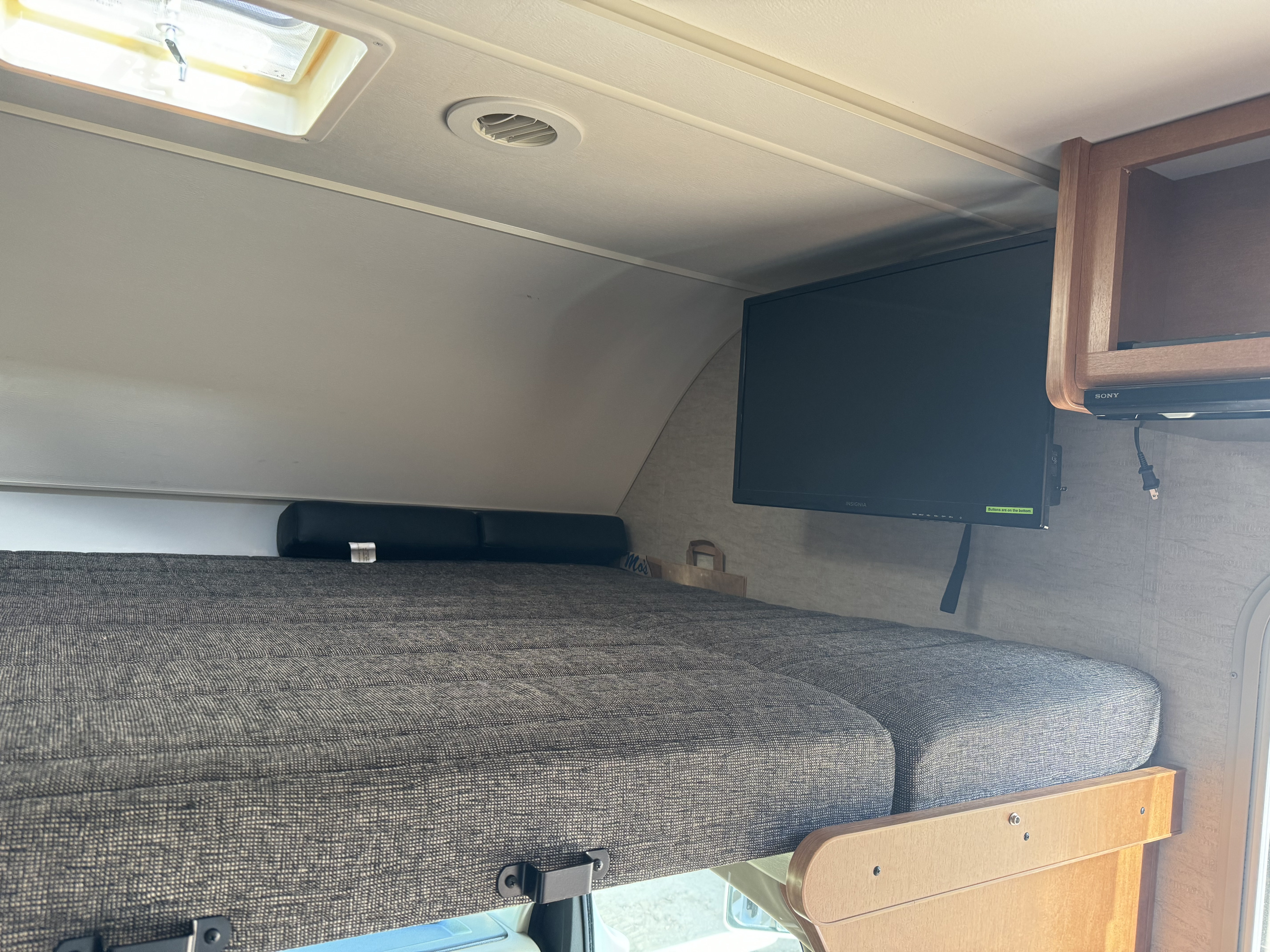 Inside an RV rental: Overcab area featuring a grey textured bed, black wall-mounted TV, and ceiling skylight for light.. Winnebago Spirit 2017