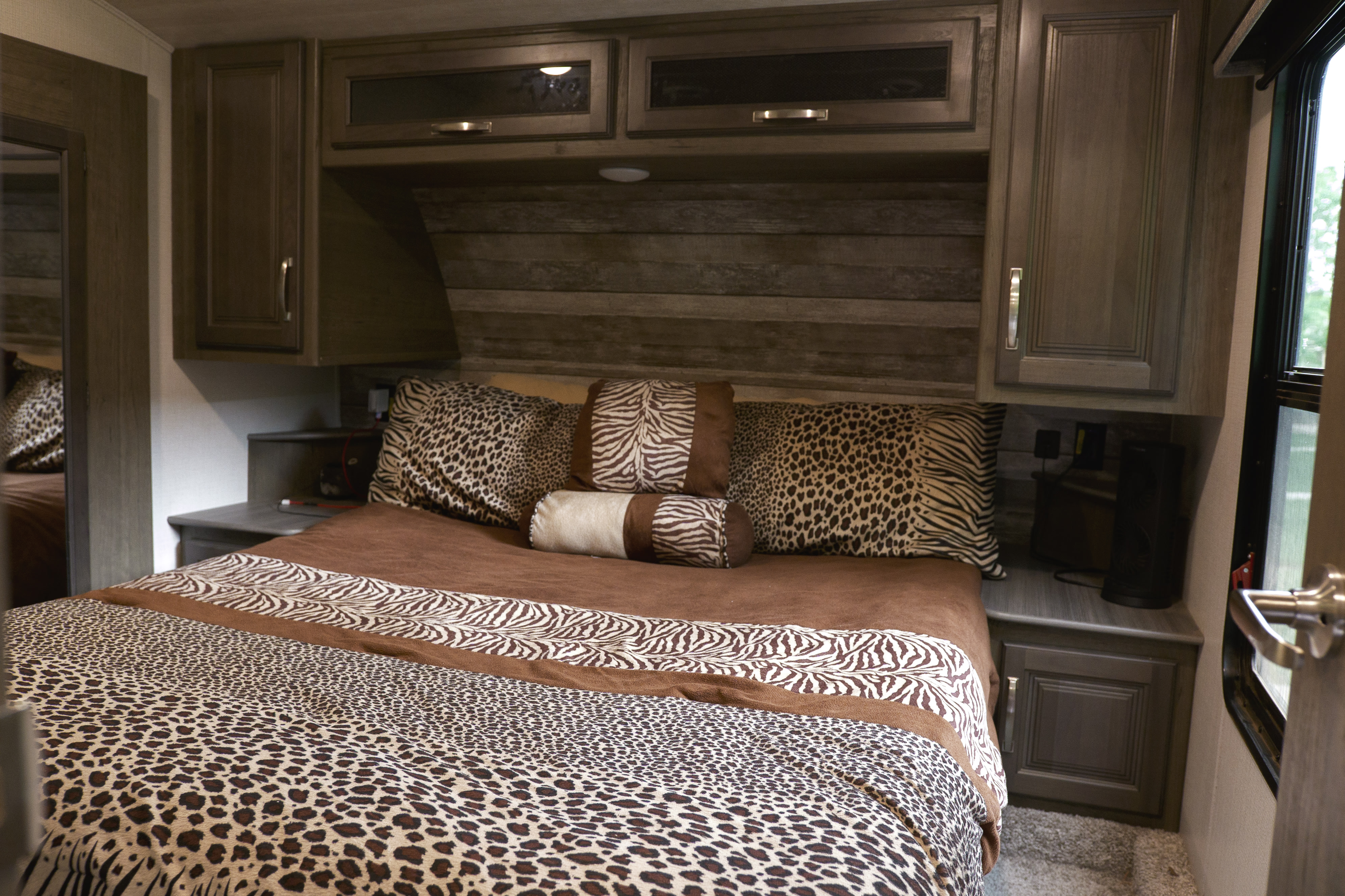 Leopard and zebra print bedding in a cozy RV rental bedroom, featuring ample storage and a bright window.. Keystone RV Cougar 2022