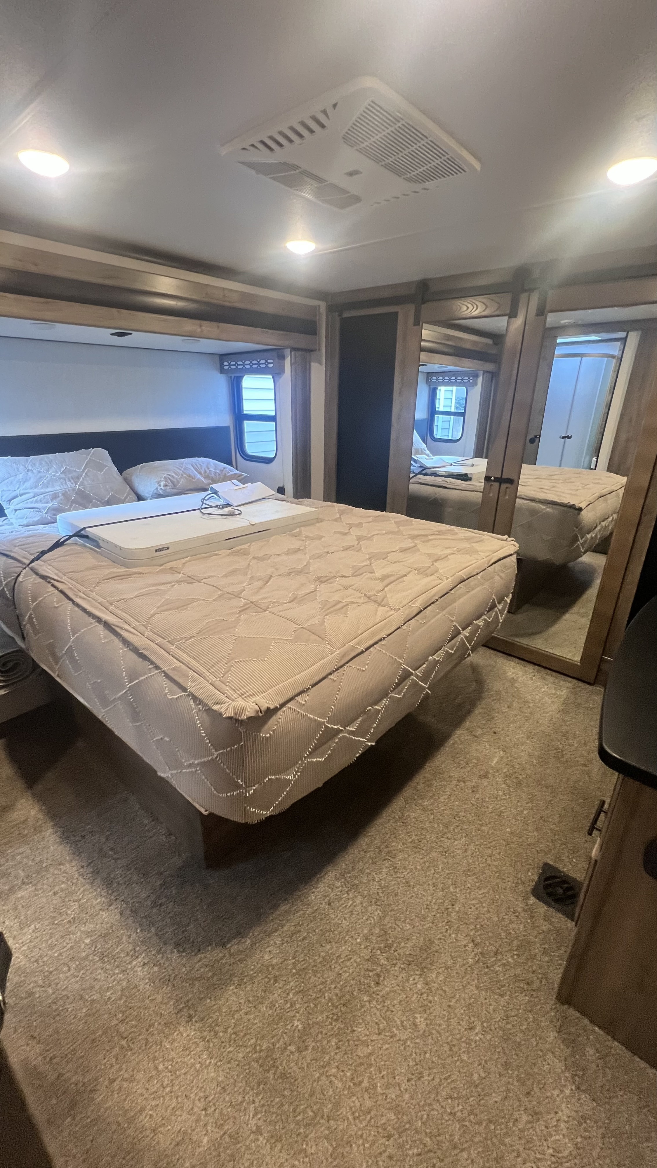 A well-lit RV rental bedroom with a beige bed, white tray, overhead AC, and mirrored closets reflecting the space.. Forest River Vengeance Vengeance Rogue Amored Toy Hauler 2022