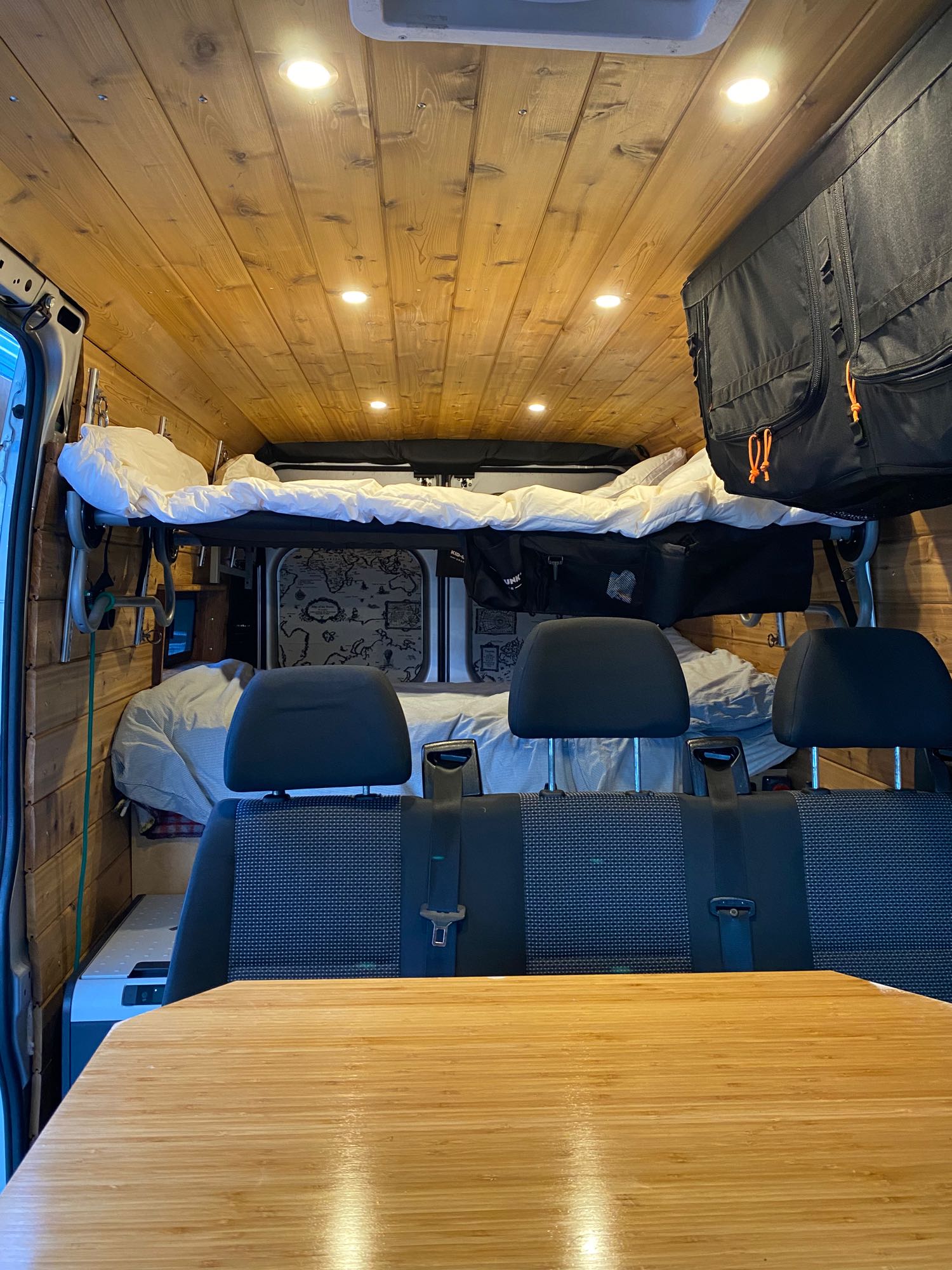 Cozy rv rental interior with wooden walls/ceiling, bunk bed, main bed, rear seats, & table. Ideal for travel.. Ram Promaster 2500 2018