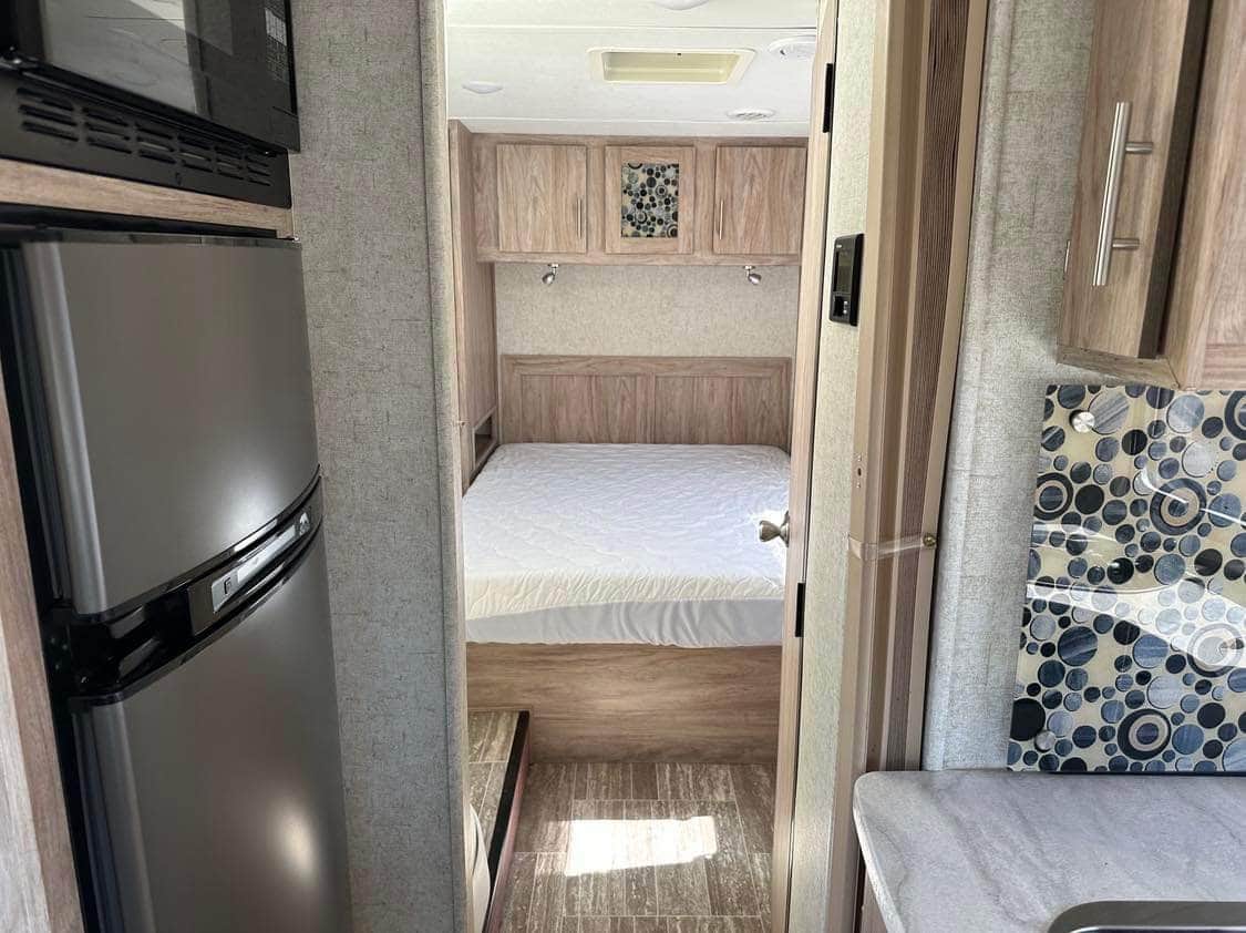 RV rental interior featuring a compact kitchen with fridge & microwave, leading to a cozy bedroom.. Forest River Sunseeker TS 2018