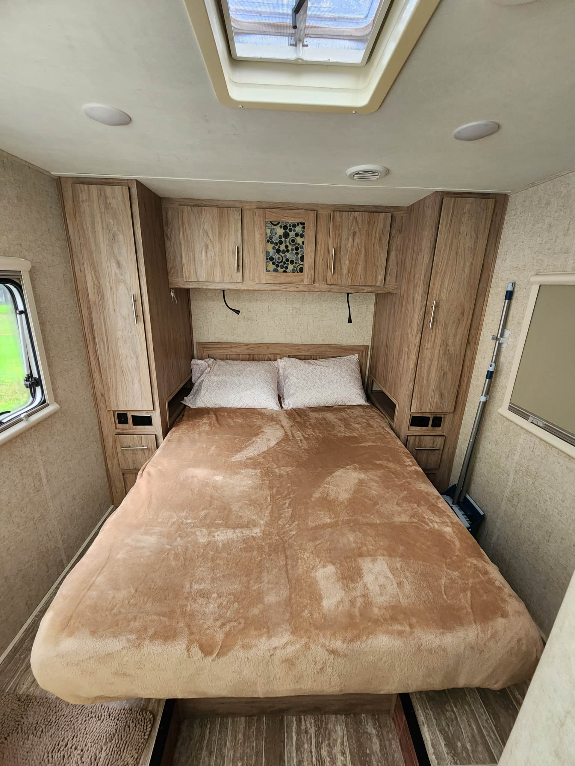 Inside an RV rental: a compact bedroom featuring a cozy bed, ample wood storage cabinets, a window, and ceiling skylight.. Forest River Sunseeker TS 2018
