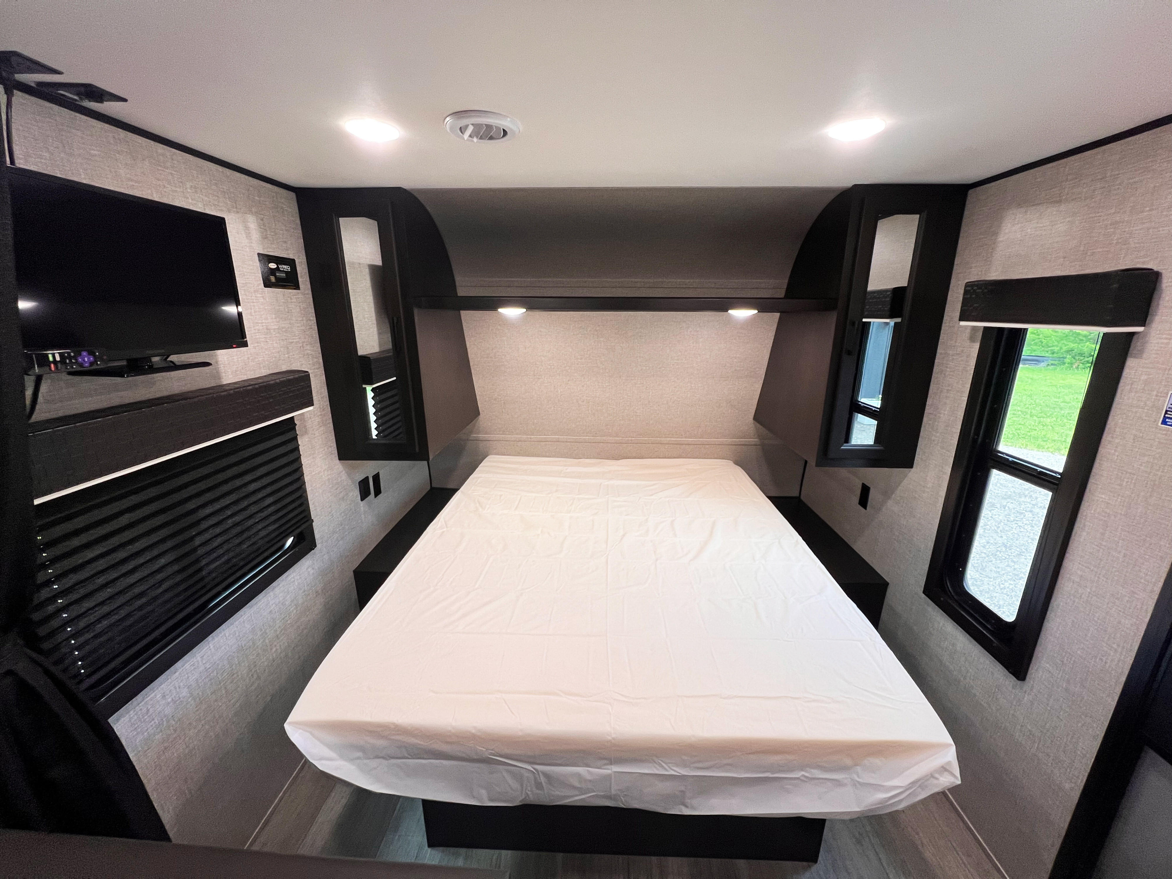 Comfortable RV rental bedroom interior with a bed, wall-mounted TV, overhead cabinets, and windows for your next journey.. Jayco Jayflight 2022