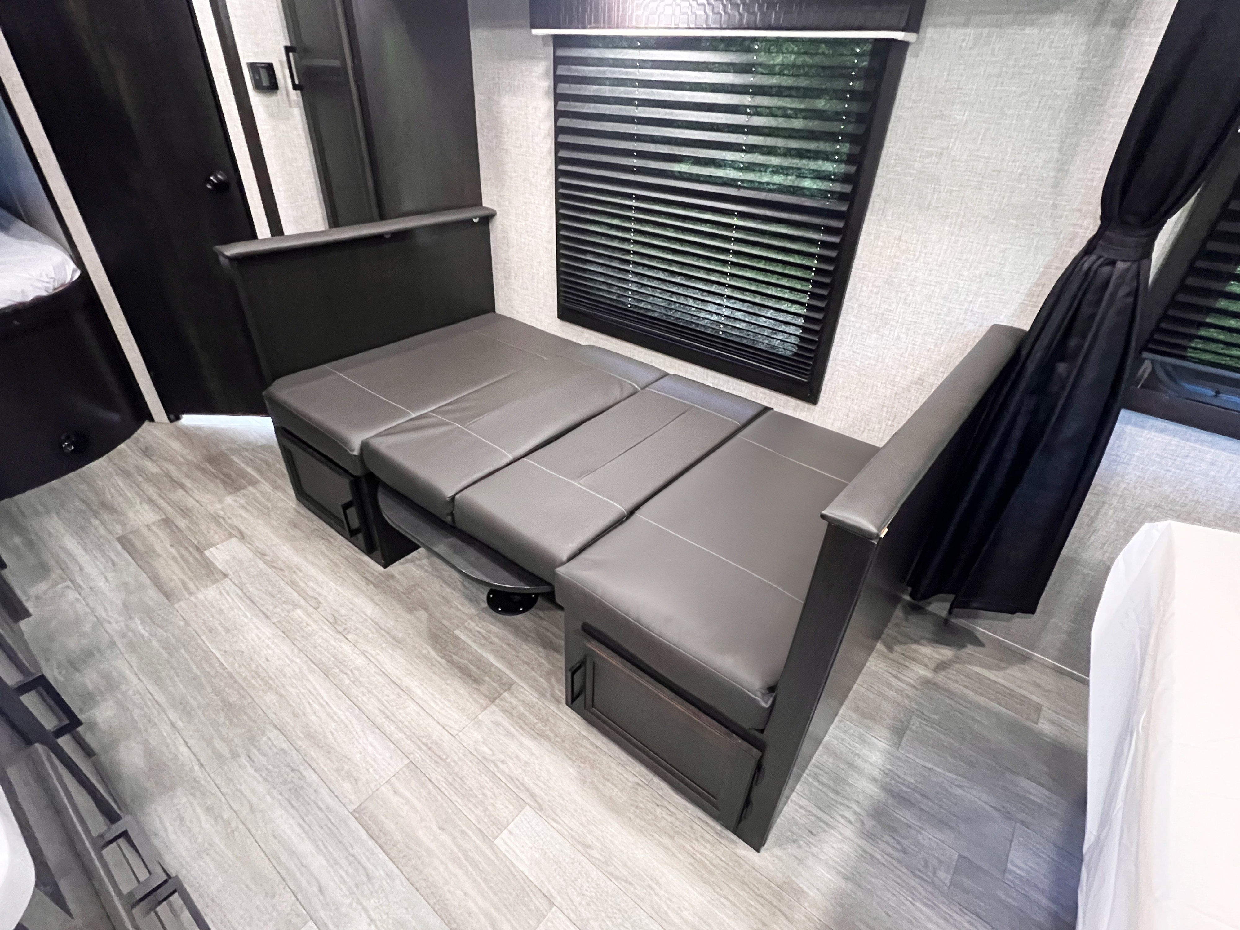 This rv rental interior features a gray convertible sofa bed with under-storage, window blinds, and wood-look flooring.. Jayco Jayflight 2022