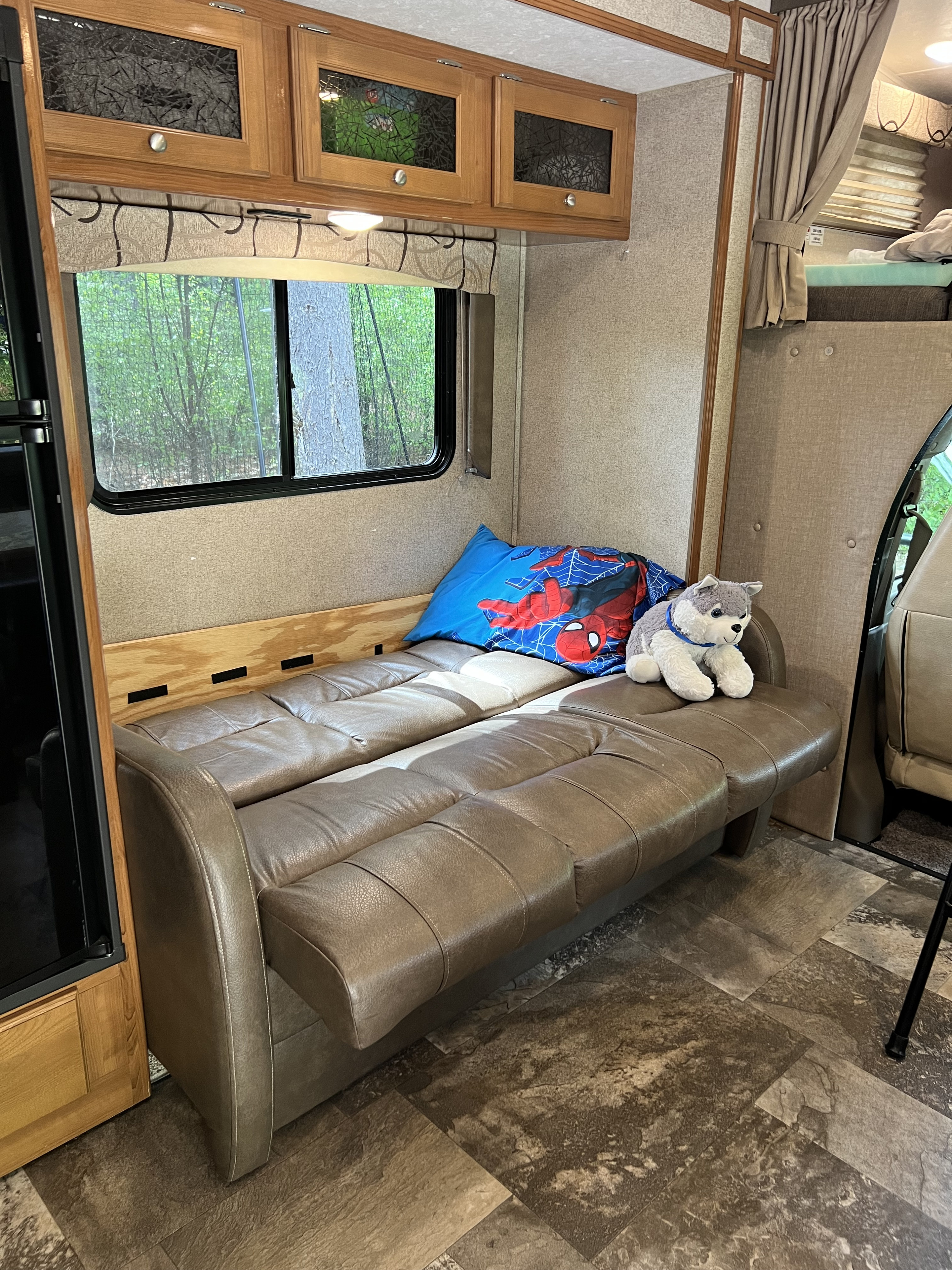 Cozy RV rental interior with a comfy faux leather sofa, window views of nature, and overhead cabinets.. Forest River Coachmen Leprechaun 2018