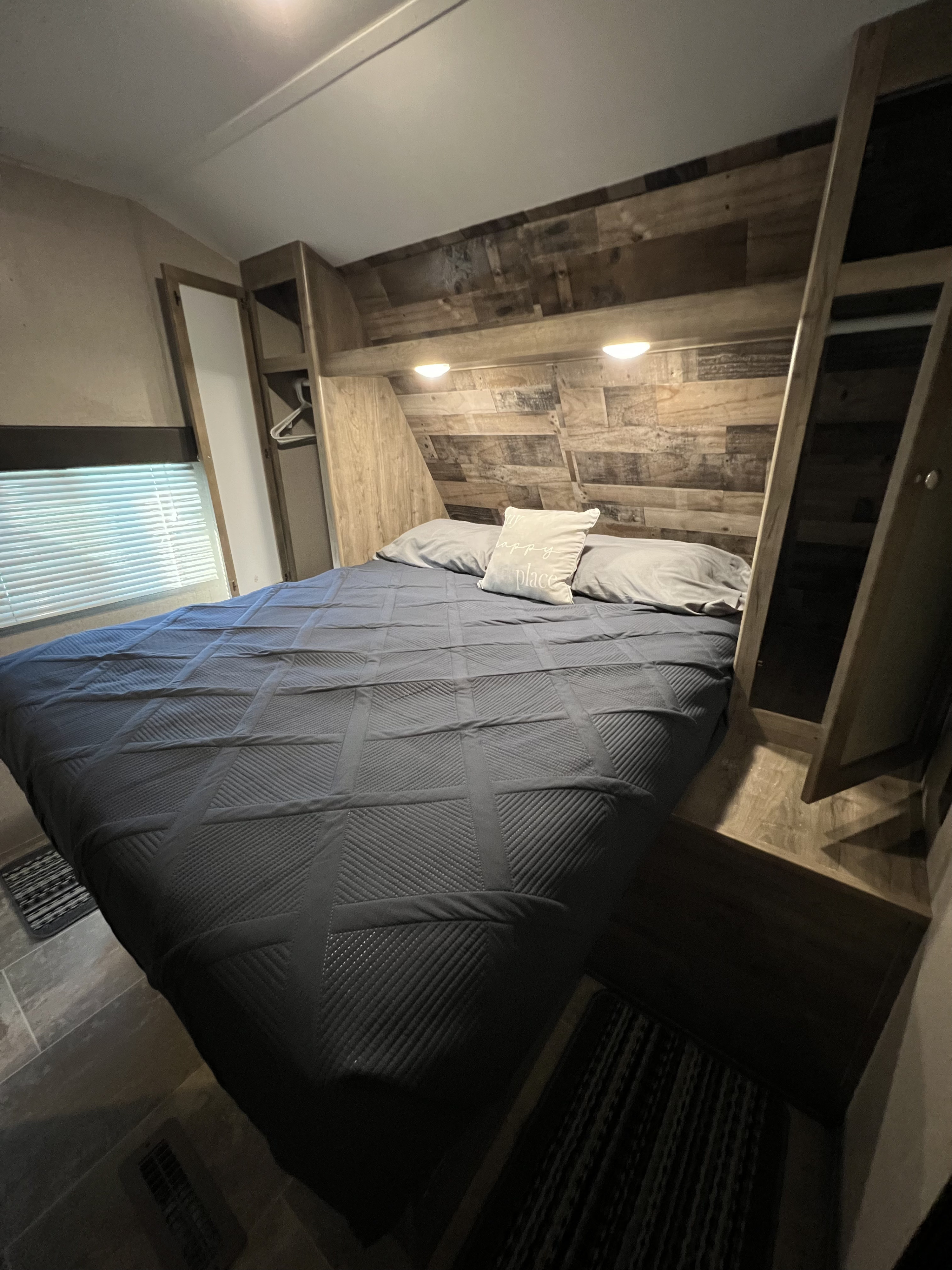 RV rental bedroom: Cozy space with a large bed, rustic wood headboard, ambient lighting, built-in storage, and window blinds.. Dutchmen Aspen Trail 2019