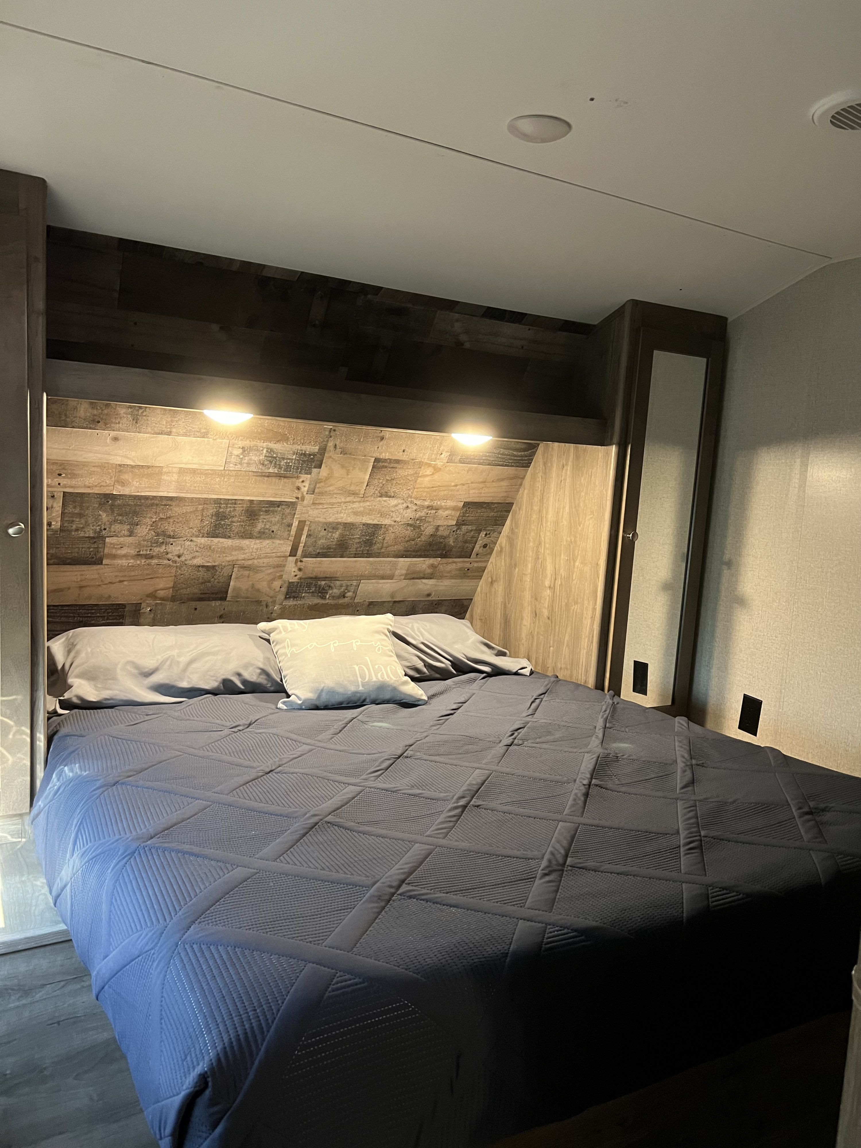 Cozy rv rental bedroom showing a bed with blue bedding, rustic wood headboard, and integrated storage.. Dutchmen Aspen Trail 2019