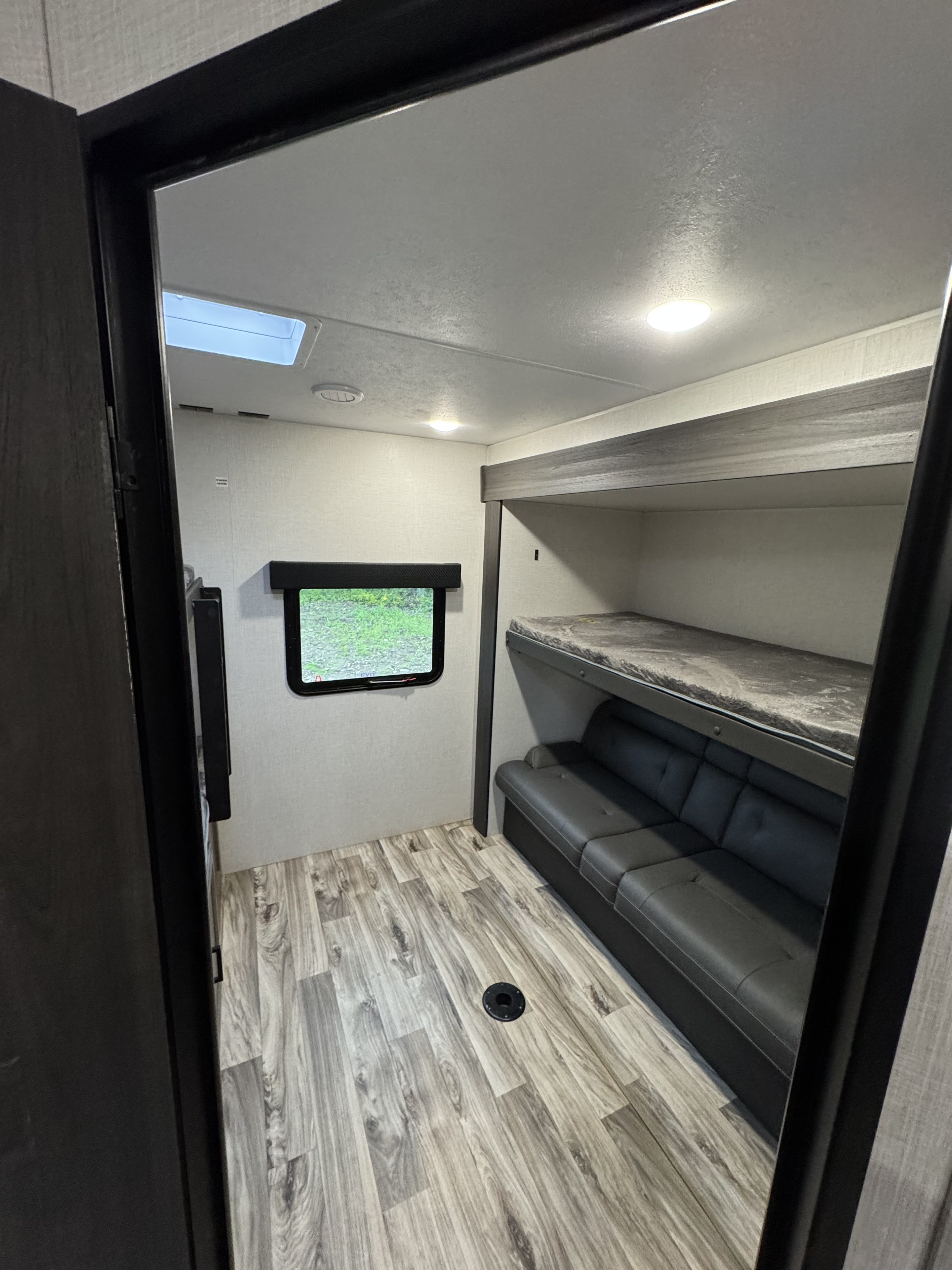 Spacious RV rental bunkhouse featuring a sofa, bunk bed, window, and wood-look flooring. Perfect for family trips!. Venture RV 327VIK 2024