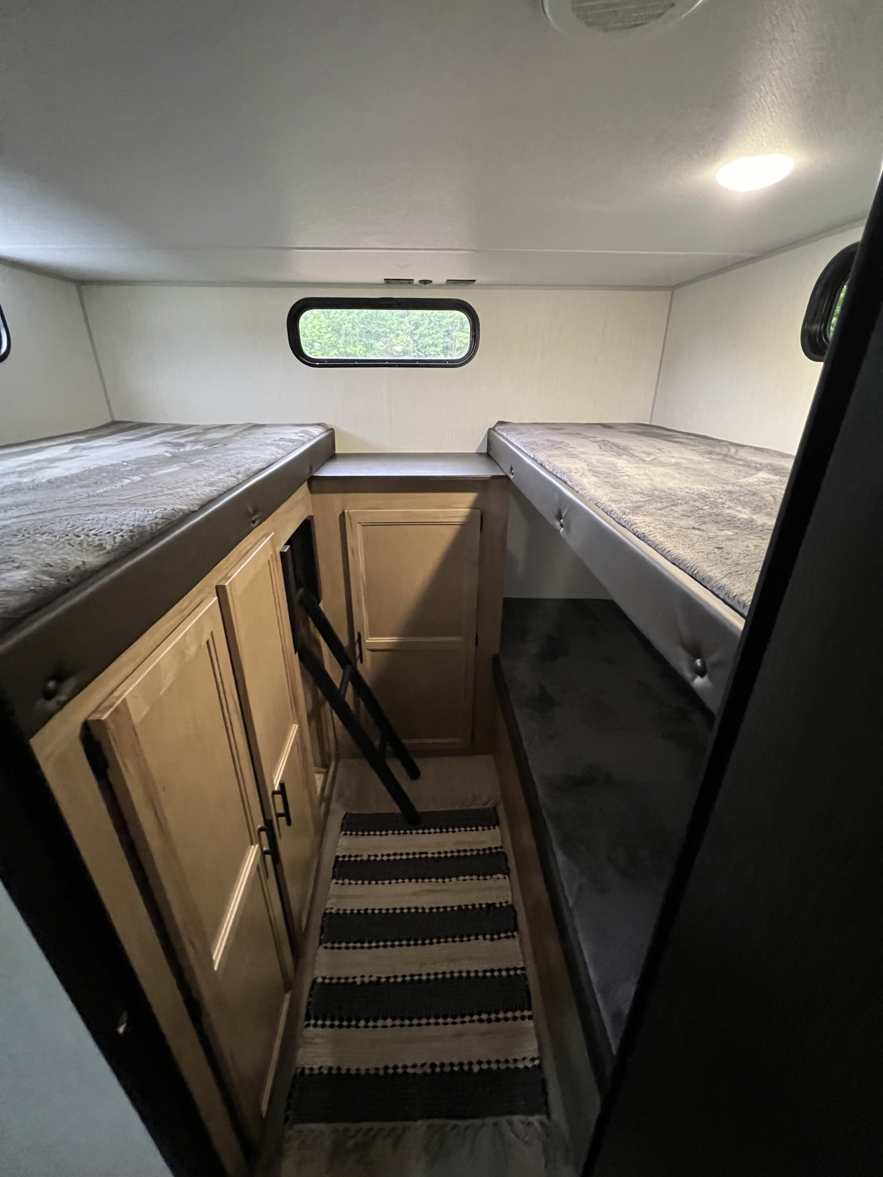 An rv rental's interior showing a narrow bunk room. Two beds, a ladder, and light wood cabinets line the compact space.. Cherokee 29TE 2025