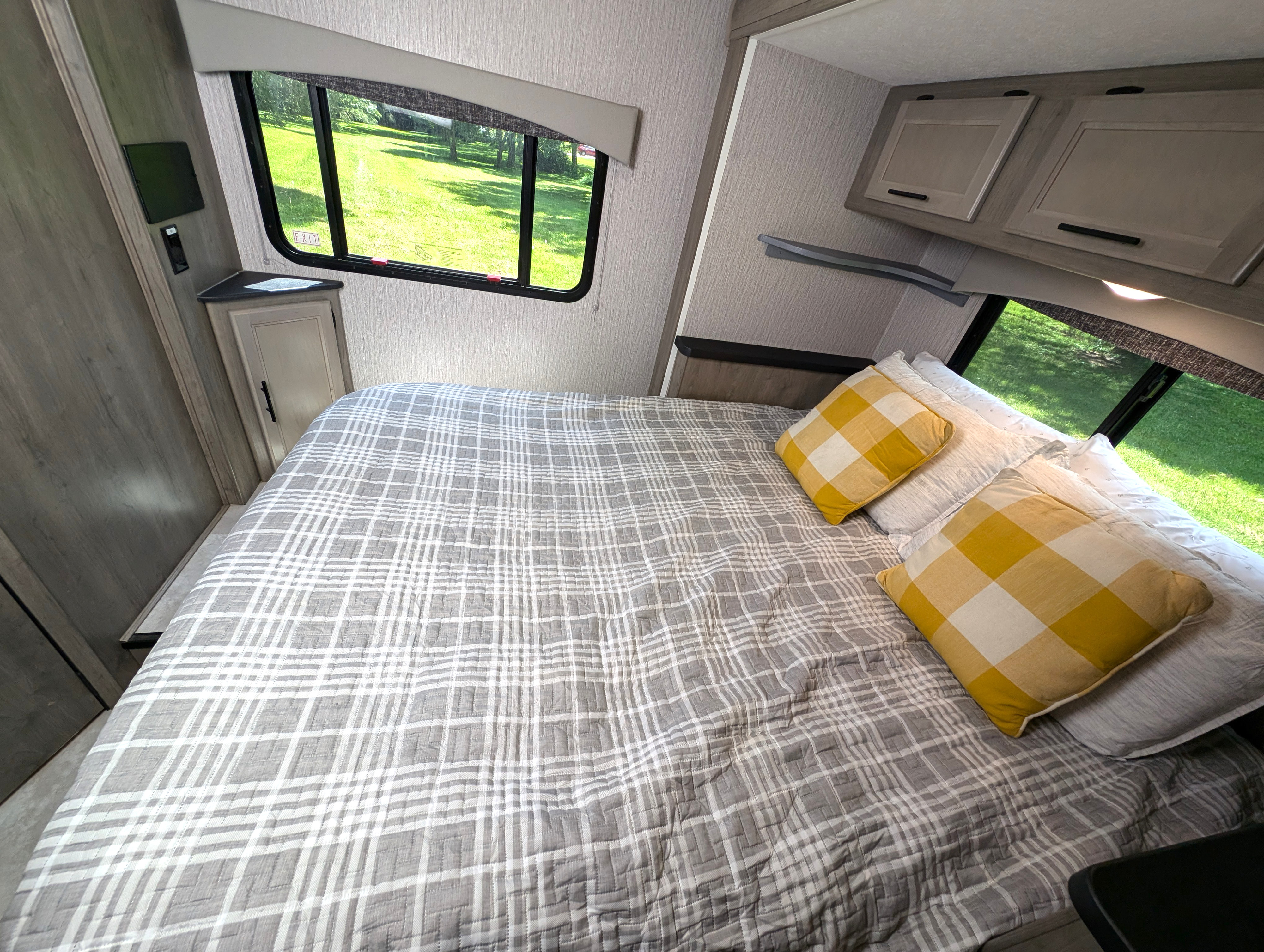 Cozy RV rental bedroom with plaid bedding, cabinets, and bright window views.. Coachman Freelander 2022
