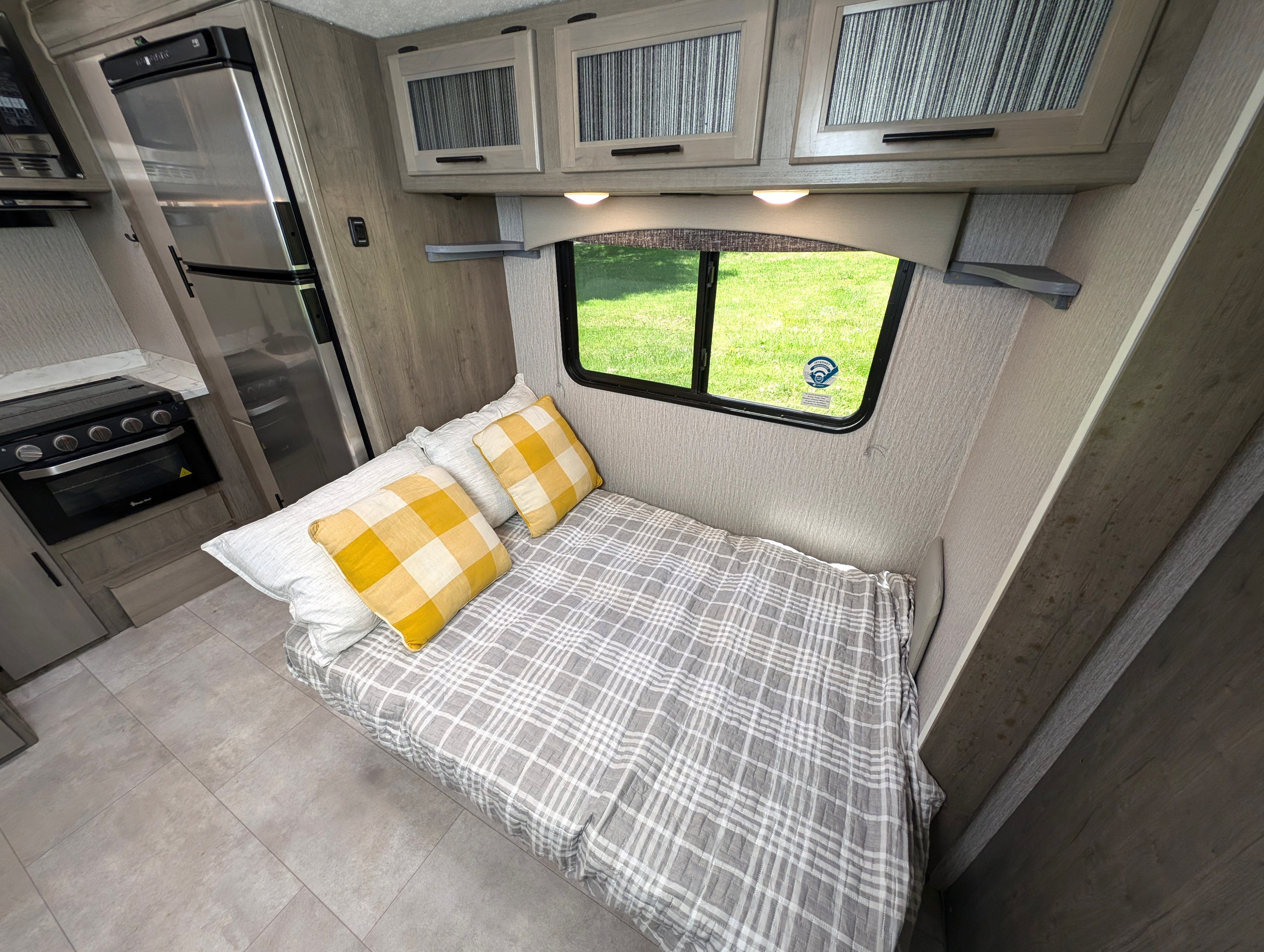 RV rental interior: cozy bed with plaid bedding, window with outdoor view, and compact kitchen appliances for travel comfort.. Coachman Freelander 2022