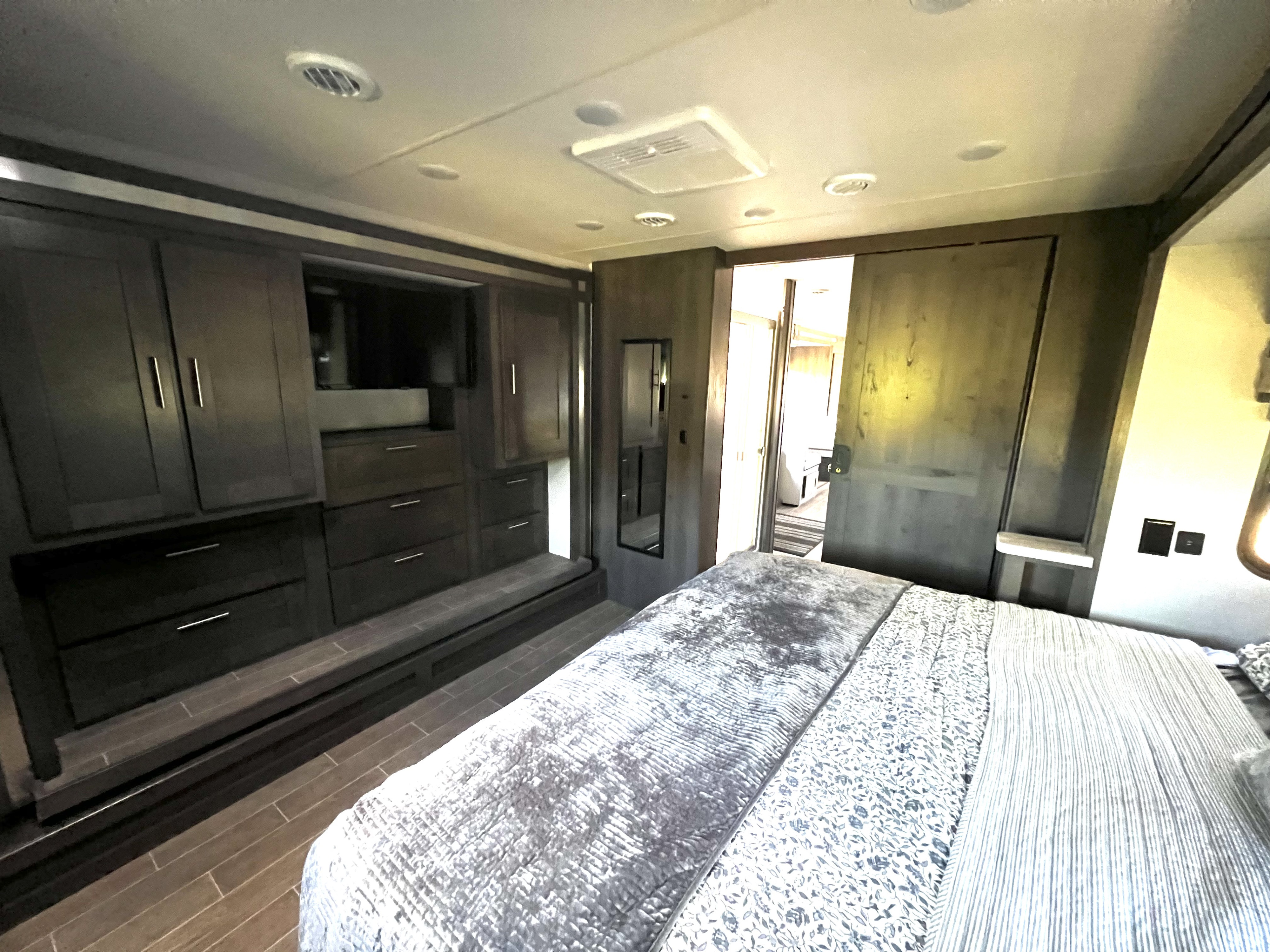 Modern RV rental bedroom features built-in dark wood cabinetry, TV, step-up storage, comfortable bed, and sliding barn door.. Georgetown GT5 2021