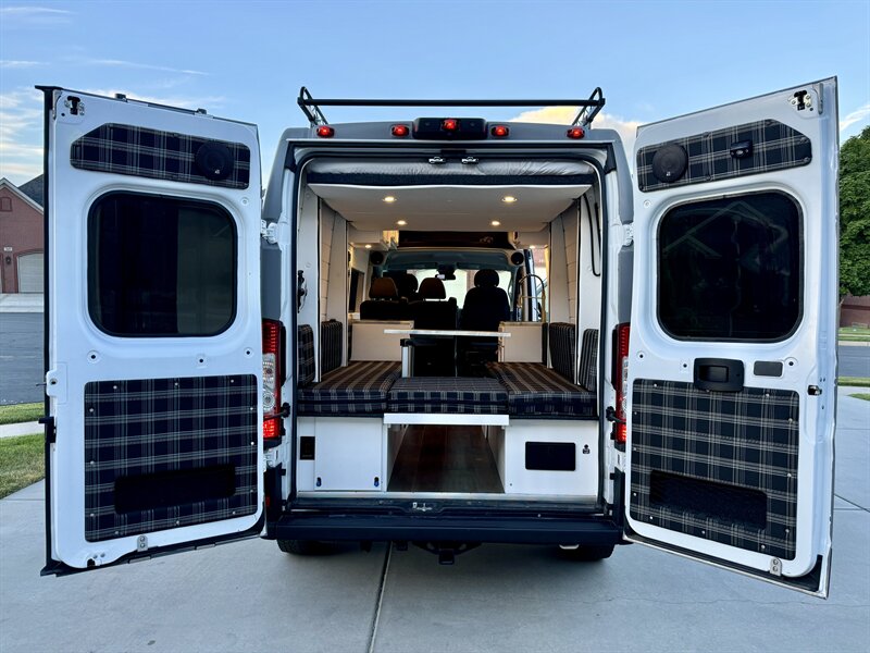 Custom RV rental camper van's open rear reveals a cozy interior with plaid cushions, seating/bed, and a small table.. Dodge Ram 1500 2021