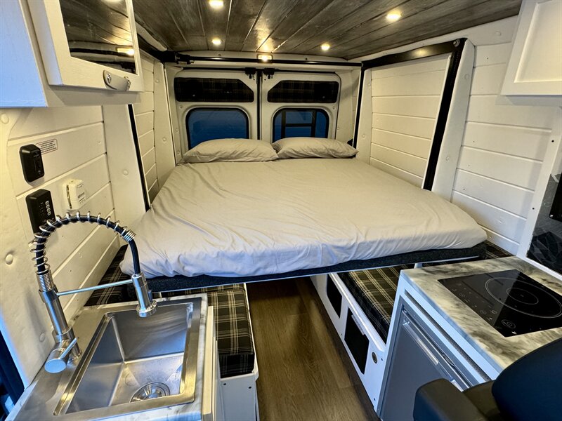 Interior of an RV rental showing a large bed at the back, with a sink on the left and a cooktop on the right.. Dodge Ram 1500 2021