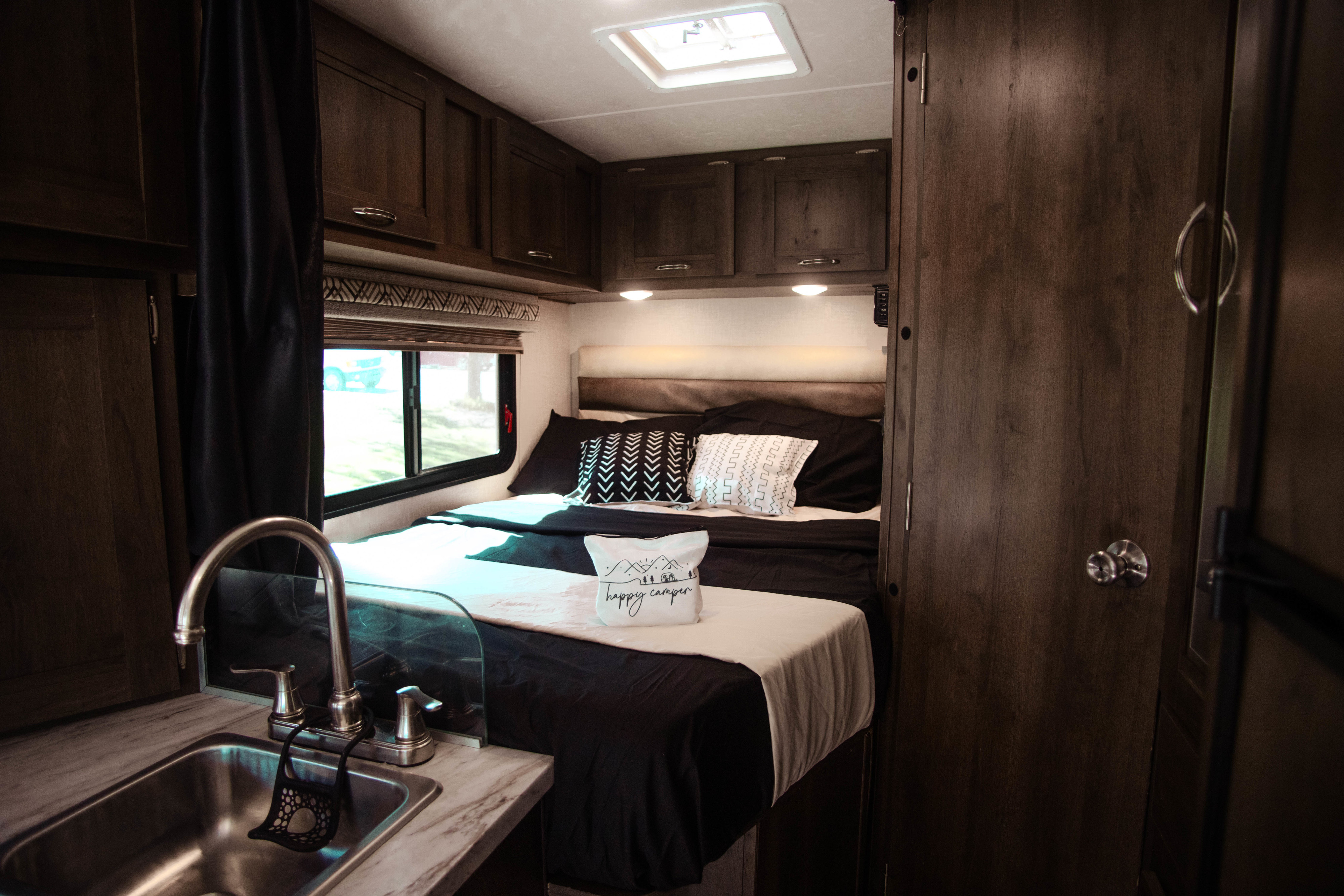 Comfortable RV rental interior features a cozy bedroom with black and white bedding, overhead storage, and a sink.. Coachmen Orion 2020