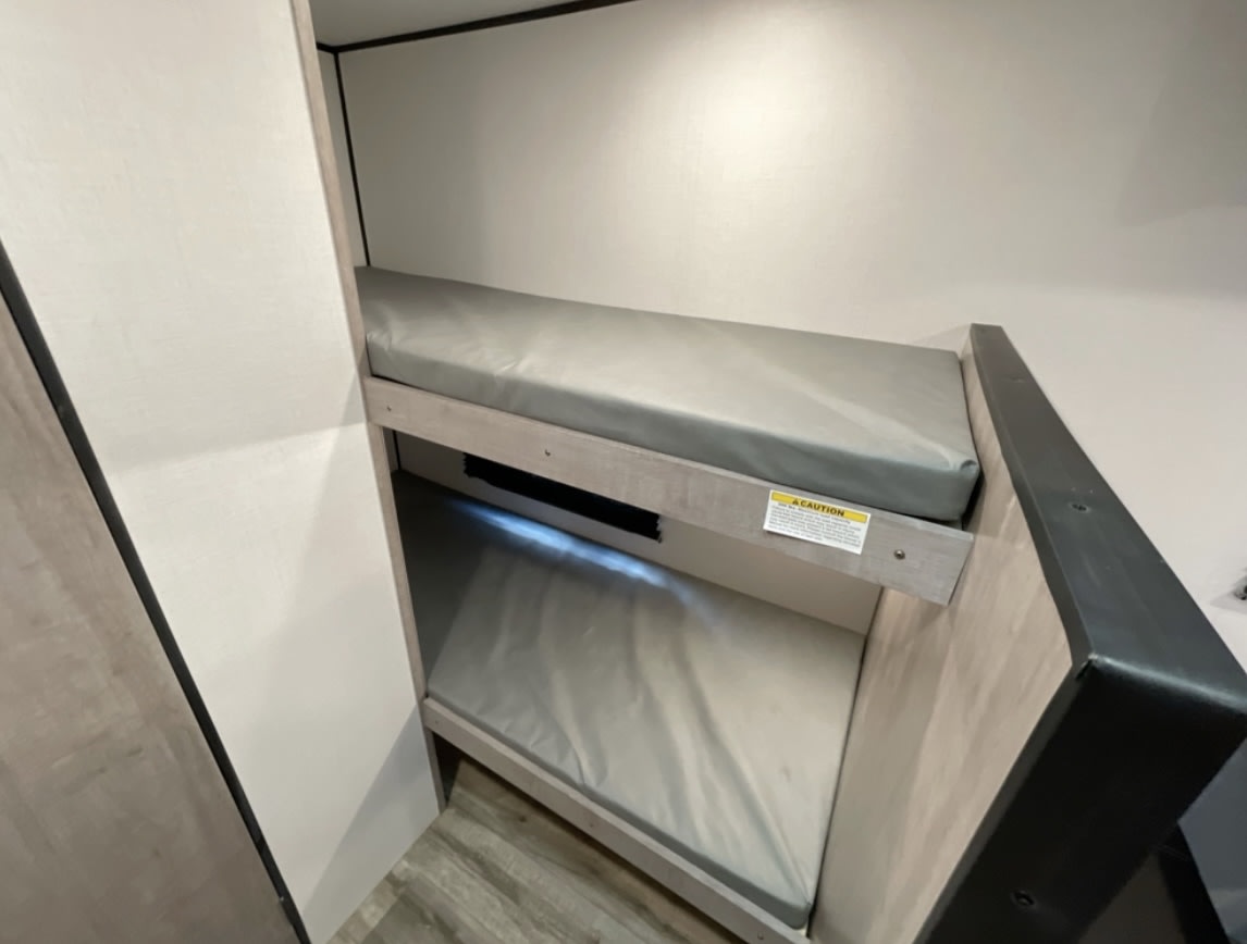 Compact bunk beds with grey mattresses and built-in lighting in an RV rental, ideal for comfortable family travel.. Coleman 17B 2023
