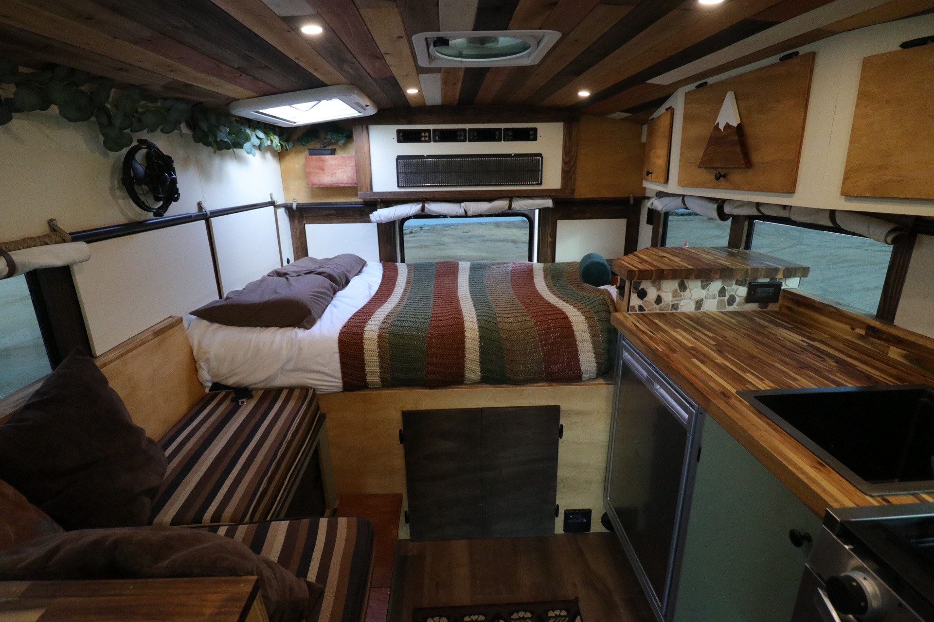 Cozy RV rental interior featuring a bed, kitchenette, seating, rustic wooden ceiling, and an outdoor view.. Chevrolet Express 2011
