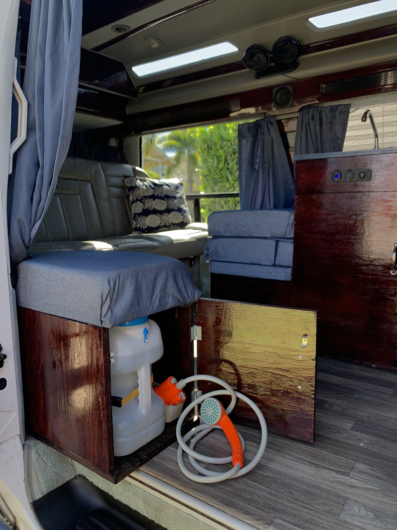 This RV rental's camper van interior features a flexible bed, compact kitchen, and portable shower setup.. Dodge B Van 1998