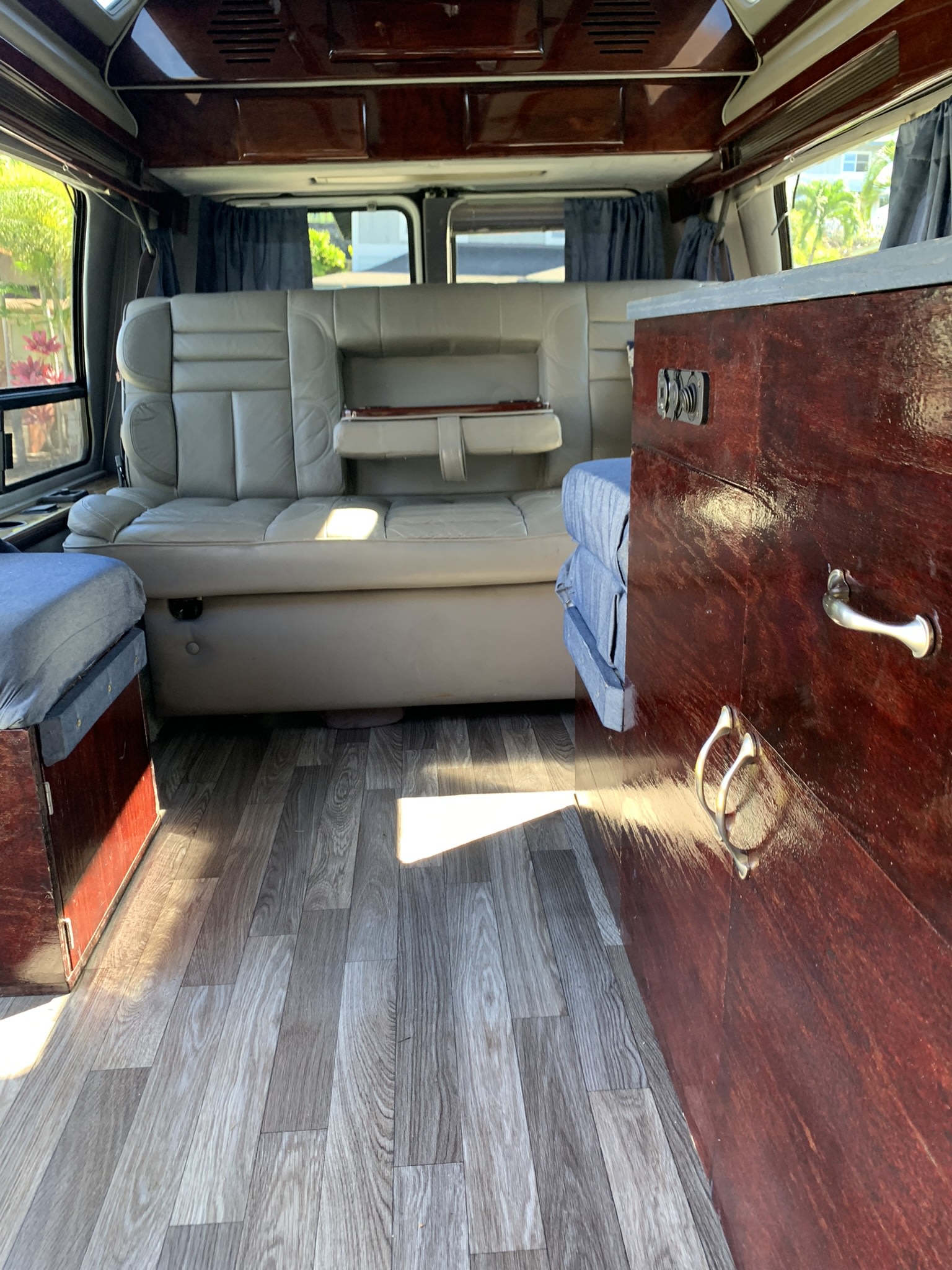 RV rental interior showing comfortable beige seating, dark wood cabinetry with chrome handles, and light wood-look flooring.. Dodge B Van 1998