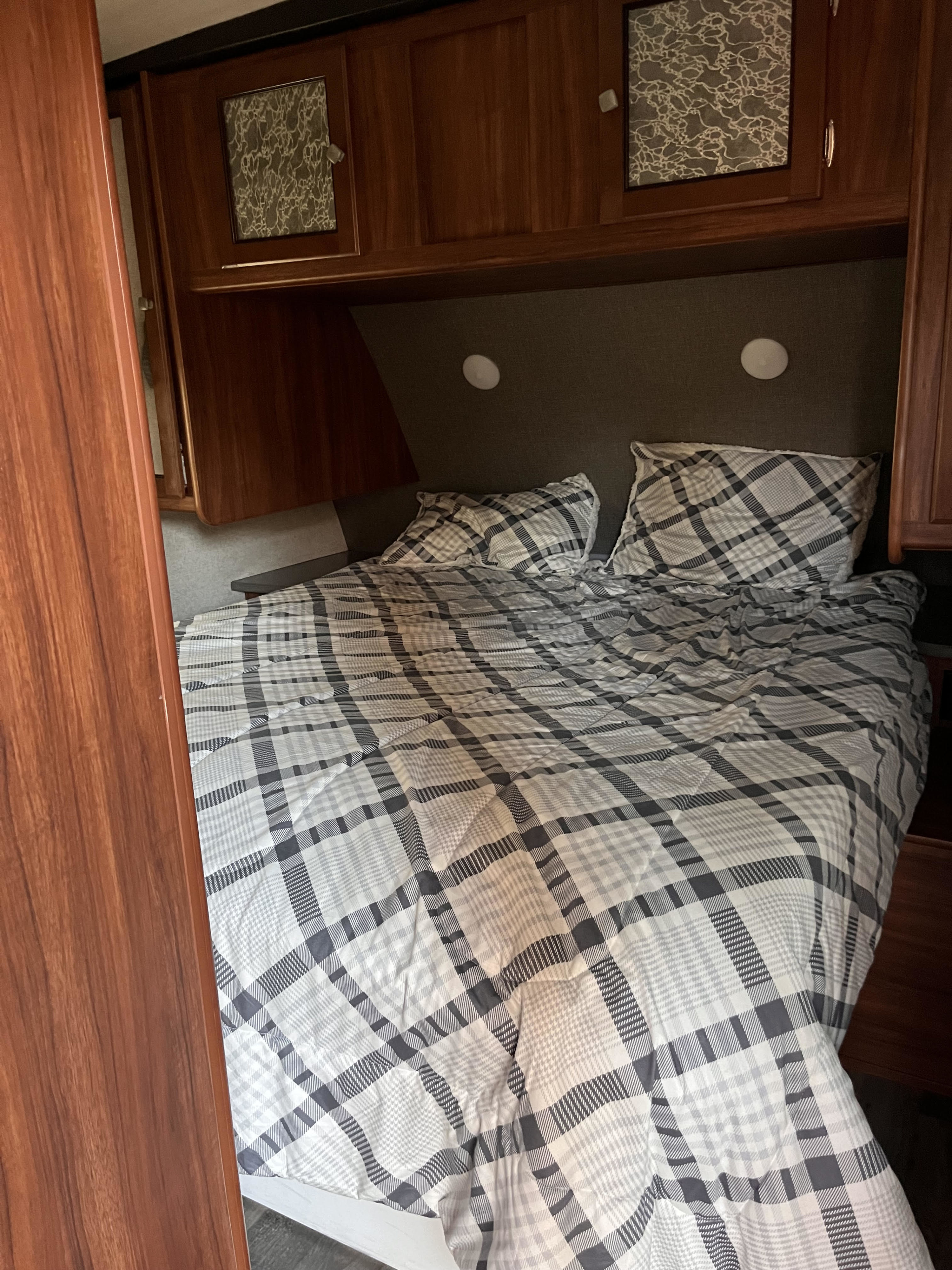 Enjoy a comfortable sleep in this RV rental's bedroom, featuring a plaid bed with overhead storage and lights.. Heartland RVs Wilderness 2018