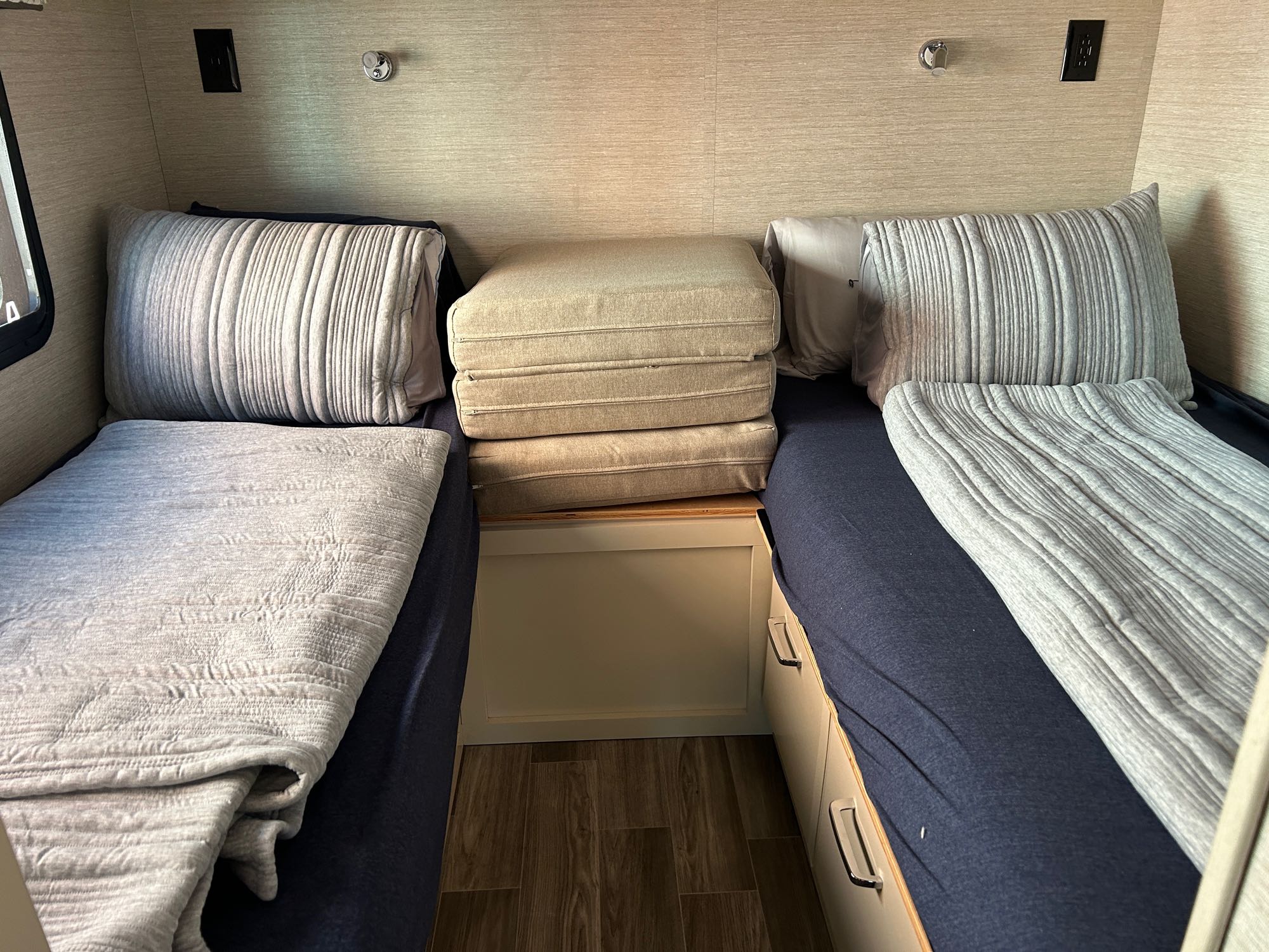 A compact RV rental sleeping space with two single beds, comfy bedding, stacked cushions, and under-bed storage.. Tiffin Midas 2022