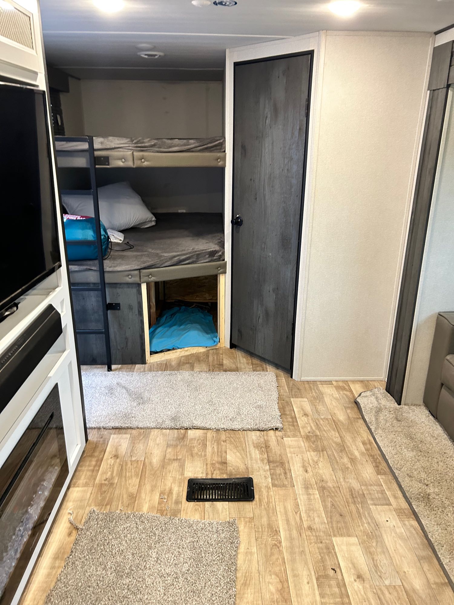 Inside an RV rental: bunk beds, entertainment center, and a closed door. Light wood floors with area rugs visible.. Keystone RV Hideout 2022