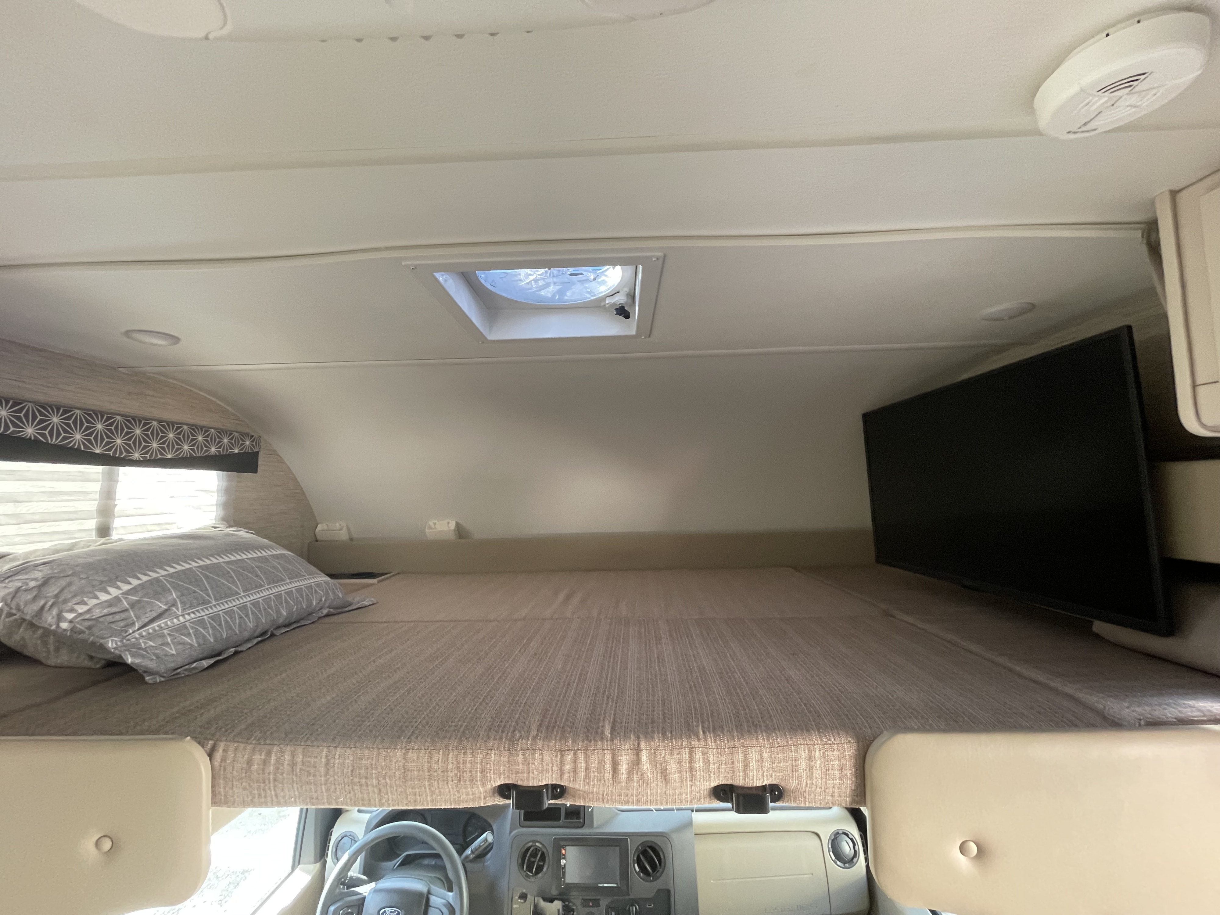 RV rental interior showing the cab-over bunk bed with a pillow, TV, and ceiling vent. View towards the driver's cabin.. Thor Freedom Elite 2022