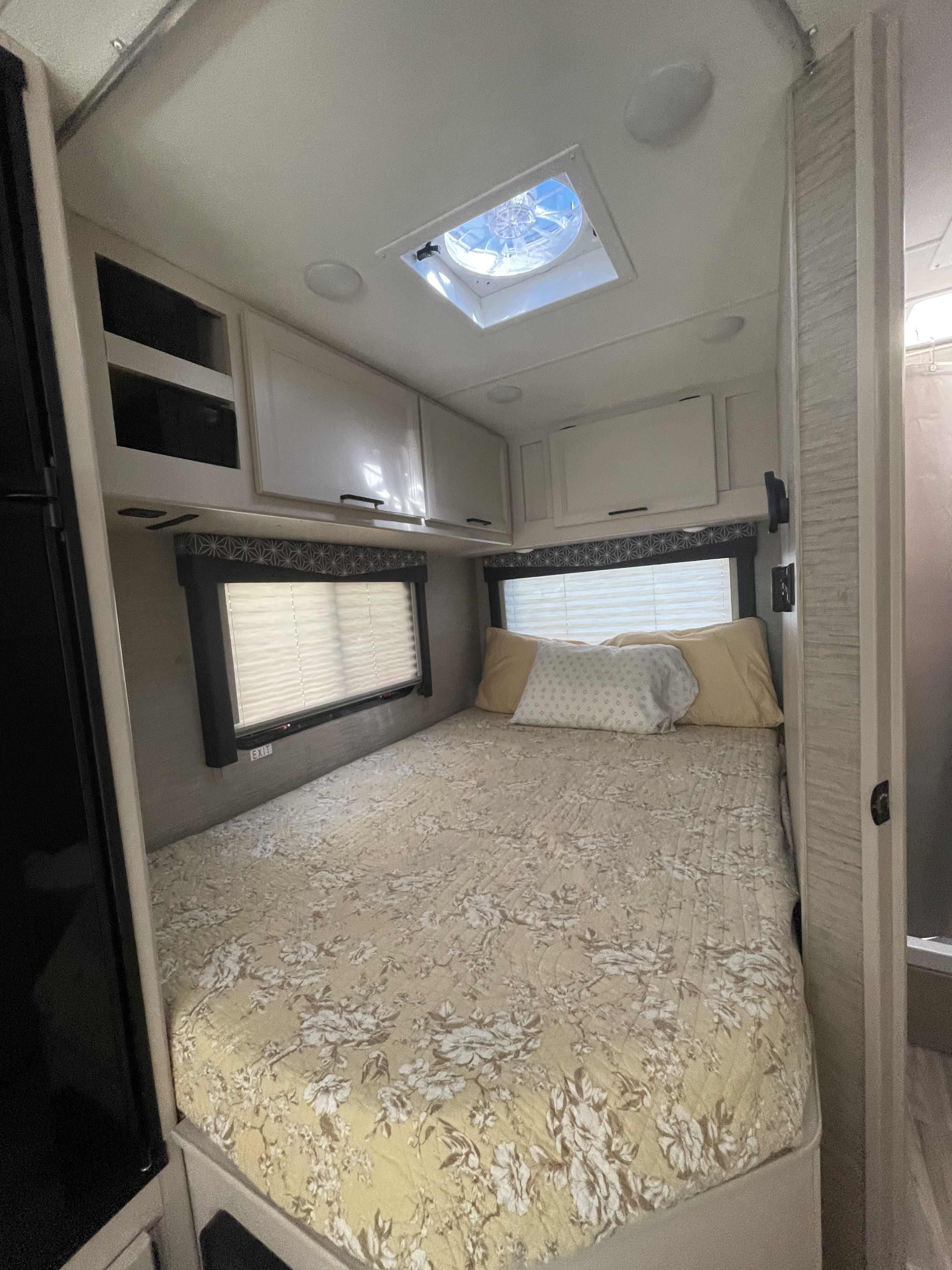 A comfortable RV rental bedroom, featuring a neatly made bed, ample overhead storage, windows, and a ceiling vent.. Thor Freedom Elite 2022