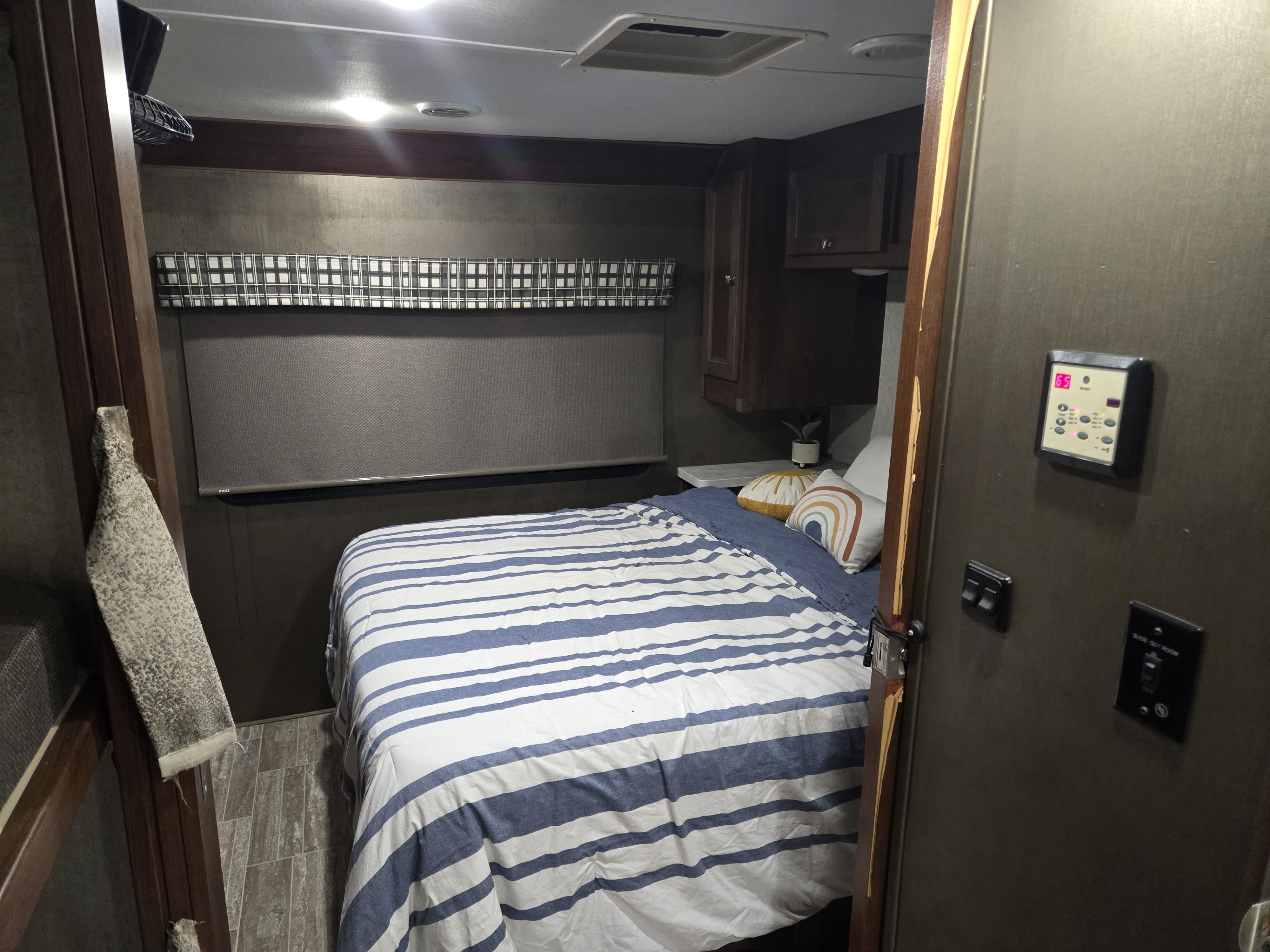 Experience a cozy RV rental interior: bedroom features striped bed, window with shade, and essential control panel.. Forest River Sunseeker LE 2020