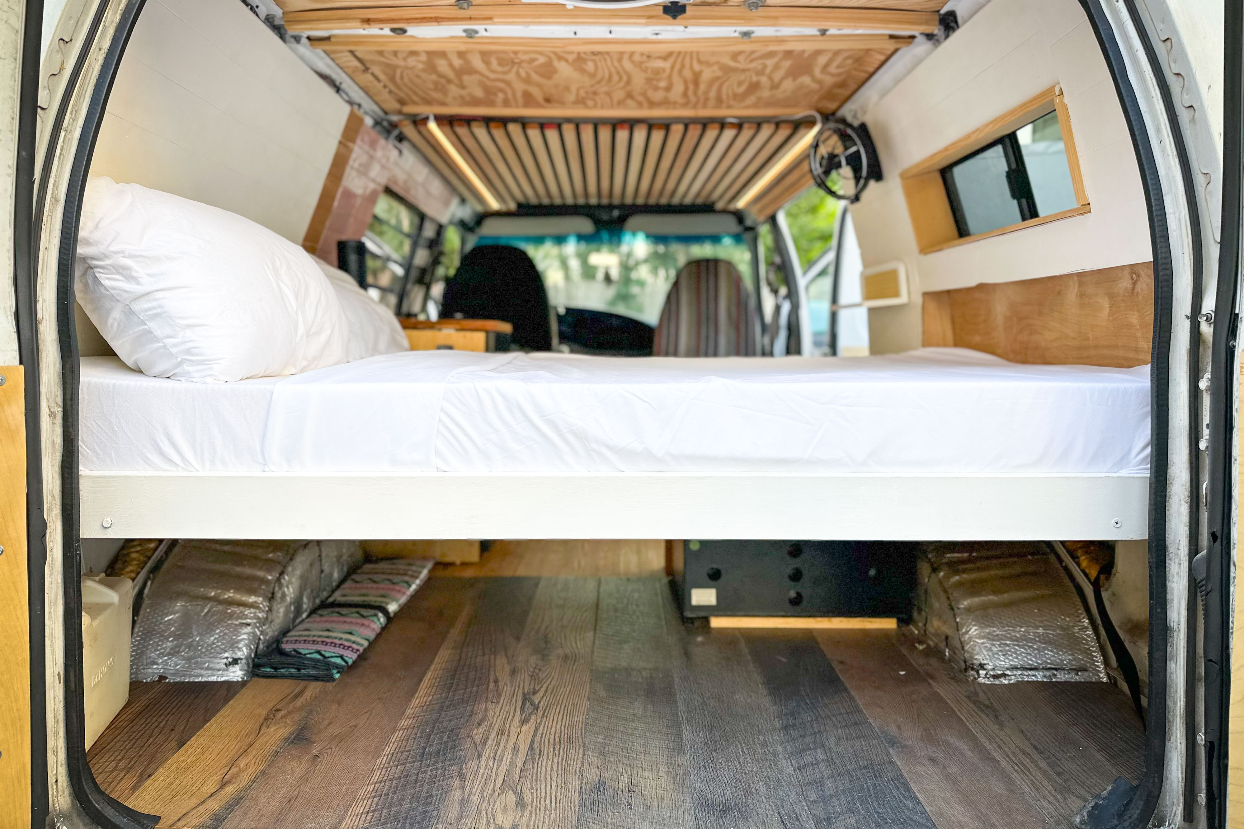 RV rental camper van bed setup. Elevated bed, under-bed storage, and wood flooring. Ideal for van life.. Ford Econoline 150 2000