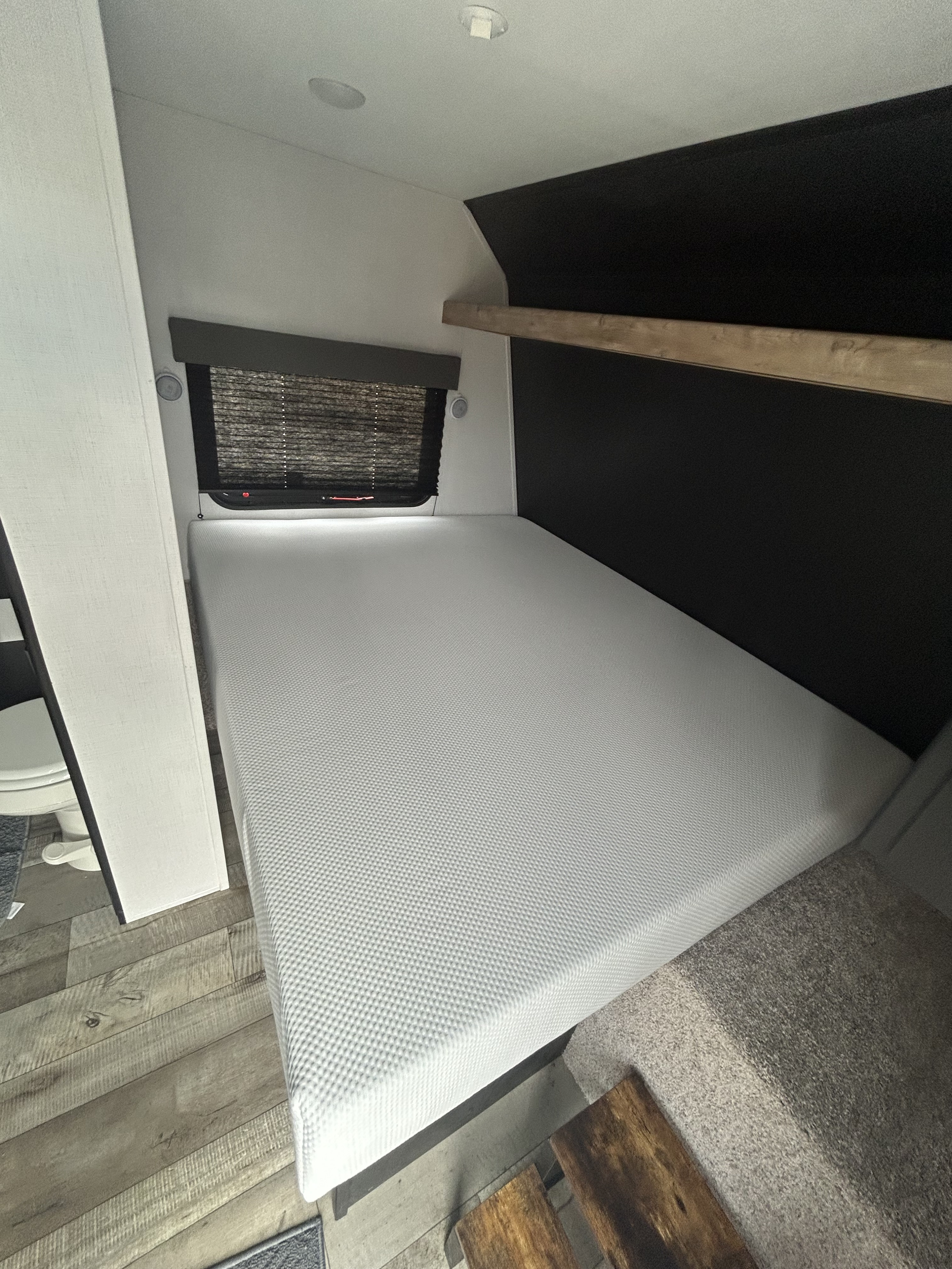 Inside a modern RV rental: a spacious bedroom with a comfortable mattress, overhead shelf, and window.. Keystone RV Springdale 2023