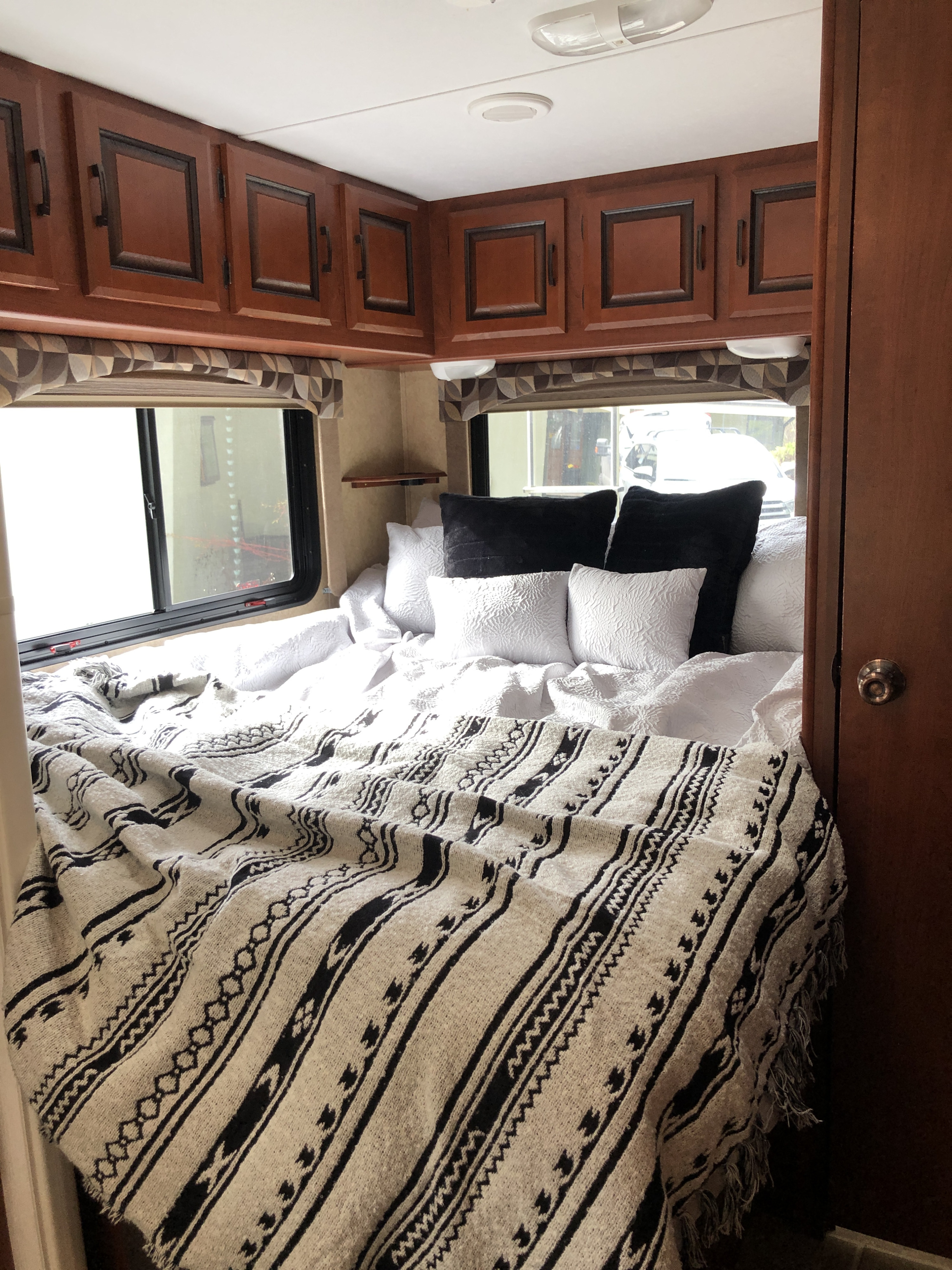 Cozy RV rental bedroom with white and black patterned bedding, overhead cabinets, and windows, perfect for comfortable travel.. Forest River Sunseeker 2011