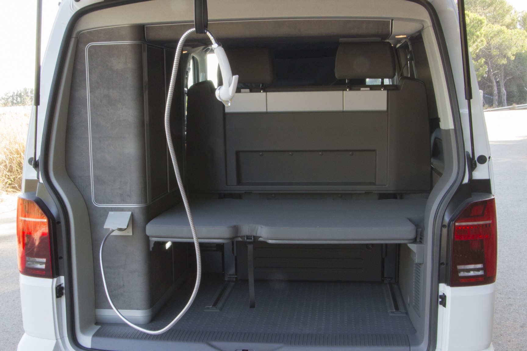 RV rental camper van's modular rear, with pulled-out bed, storage, and outdoor shower hose. Ready for adventures!. Volkswagen California Ocean 2023