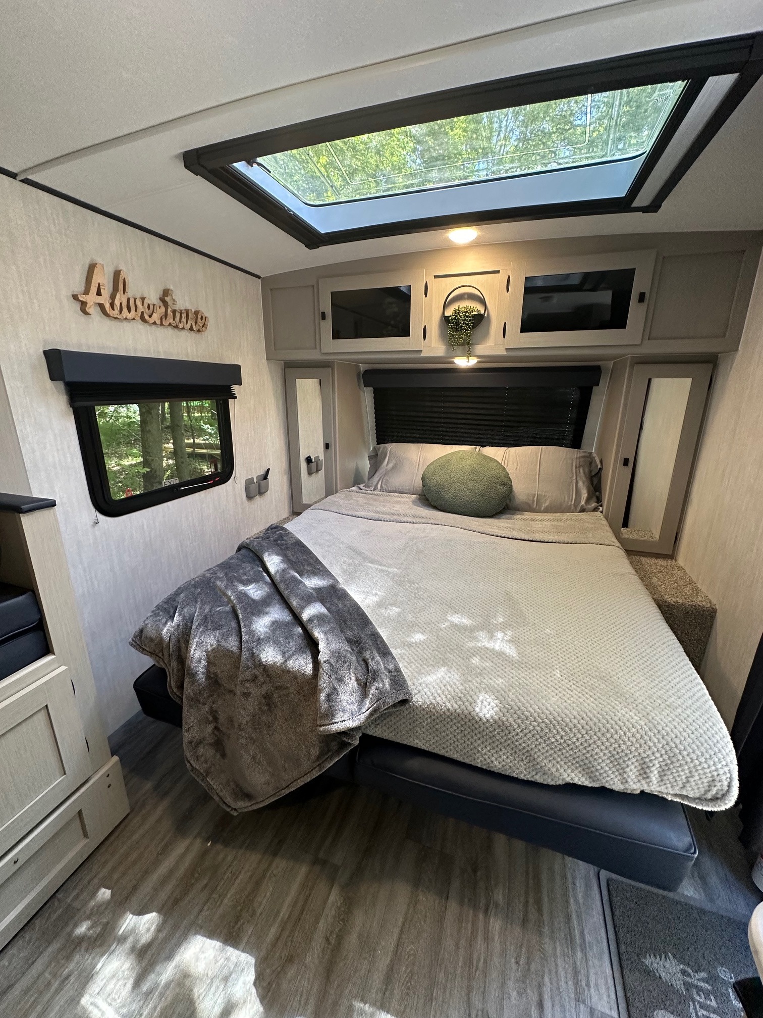 Cozy RV rental bedroom featuring a large bed, overhead cabinets, a skylight, and a window with tree views. Perfect for your adventure.. Coachmen Apex Nano 2024